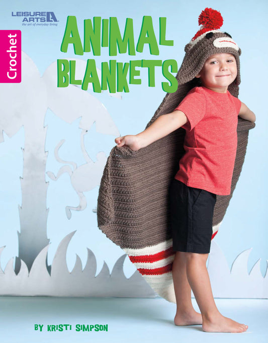 A smiling child in a red shirt and black shorts stands barefoot on a blue floor, wearing a Crochet Animal Blanket made with medium weight yarn and fun appliqué accents. White animal cutouts surround them. Leisure Arts branding is shown.