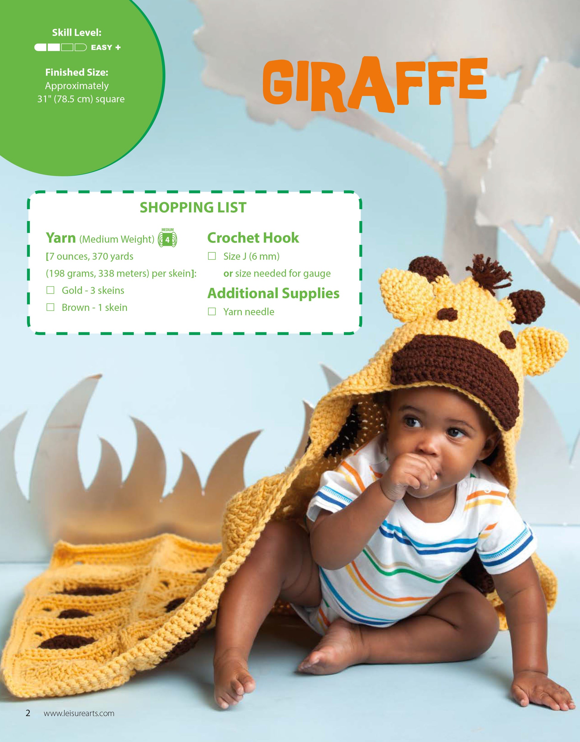 A baby sits on the floor wrapped in a yellow and brown giraffe hooded blanket from Leisure Arts’ Crochet Animal Blankets collection, featuring crocheted ears and horns. Light blue and tan decorative trees appear in the background.