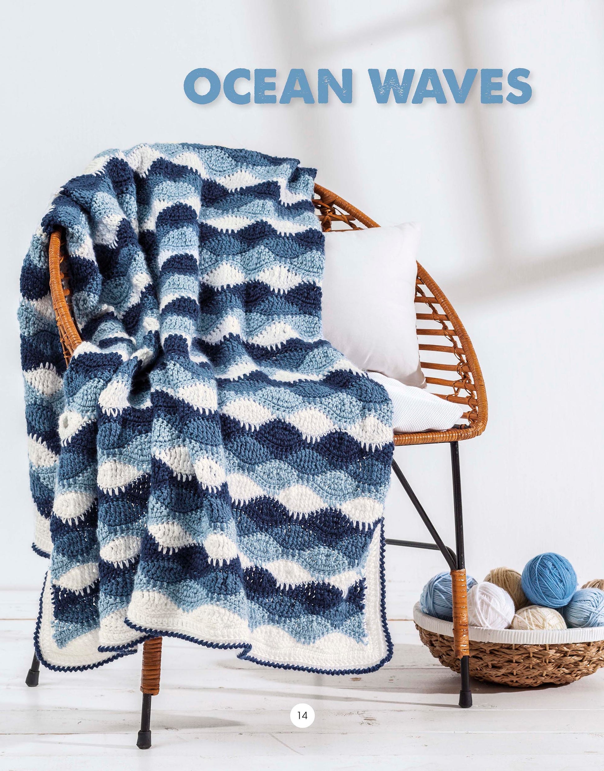 A blue and white Graphic Pattern Afghans blanket by Leisure Arts drapes over a wicker chair with a white cushion, adding geometric style to your decor. A basket of blue, white, and tan yarn sits nearby. Text above reads OCEAN WAVES.