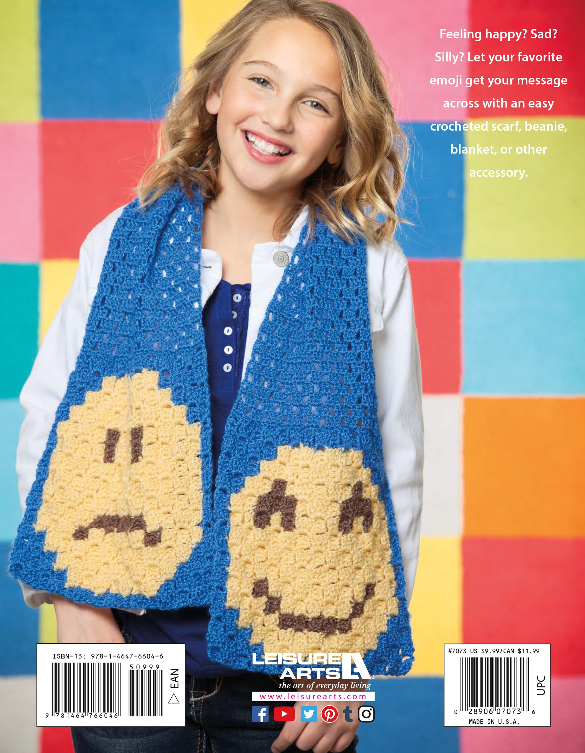 A smiling girl stands before a colorful checkered backdrop, modeling the Leisure Arts Emoji Crochet scarf in blue, featuring large happy and sad yellow emojis—a perfect beginner project from the Emoji Crochet collection.