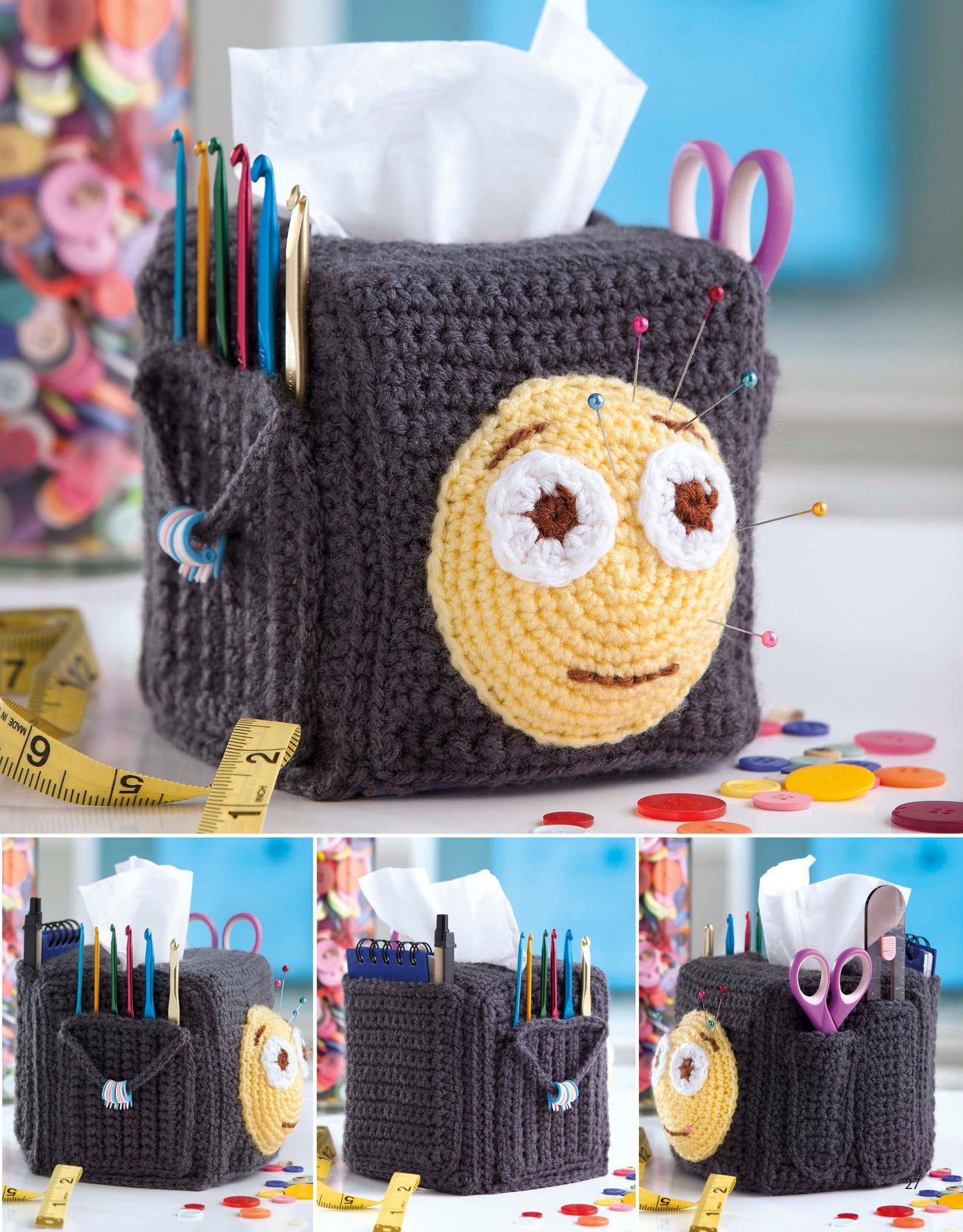 The Emoji Crochet by Leisure Arts is a gray crocheted tissue box cover with a yellow smiley face. It doubles as a craft organizer for scissors, crochet hooks, and pins, with buttons and a tape measure scattered nearby.