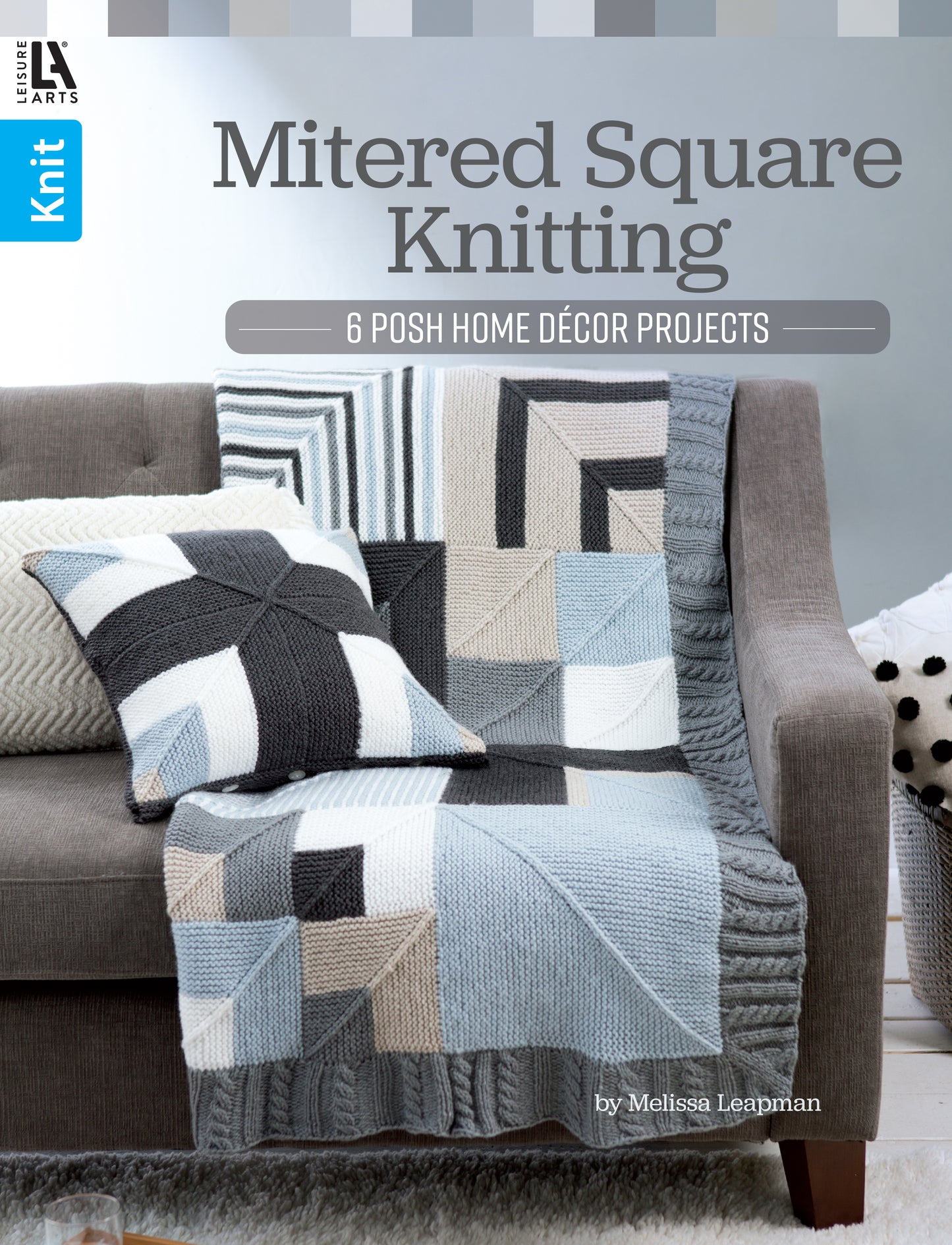 A gray sofa displays a black, white, gray, and beige mitered square knit pillow and matching garter stitch blanket draped over the armrest. The image is the cover for "Mitered Square Knitting Digital Download" by Leisure Arts.