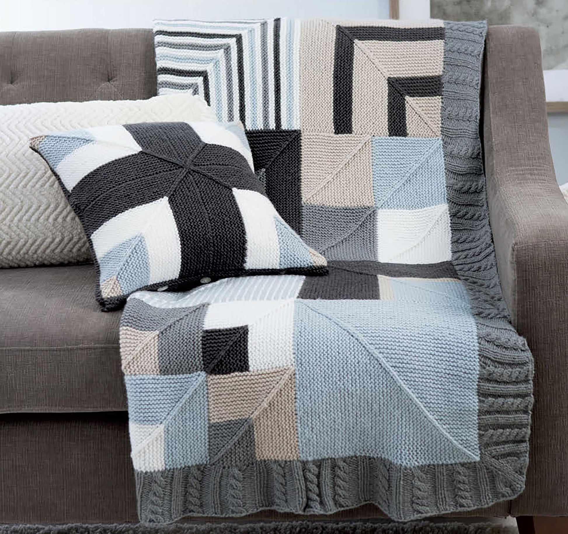 The Leisure Arts Mitered Square Knitting Digital Download features a modern garter stitch blanket and matching geometric pillow in gray, blue, beige, and white, draped over a gray sofa with an additional textured cushion in the background.