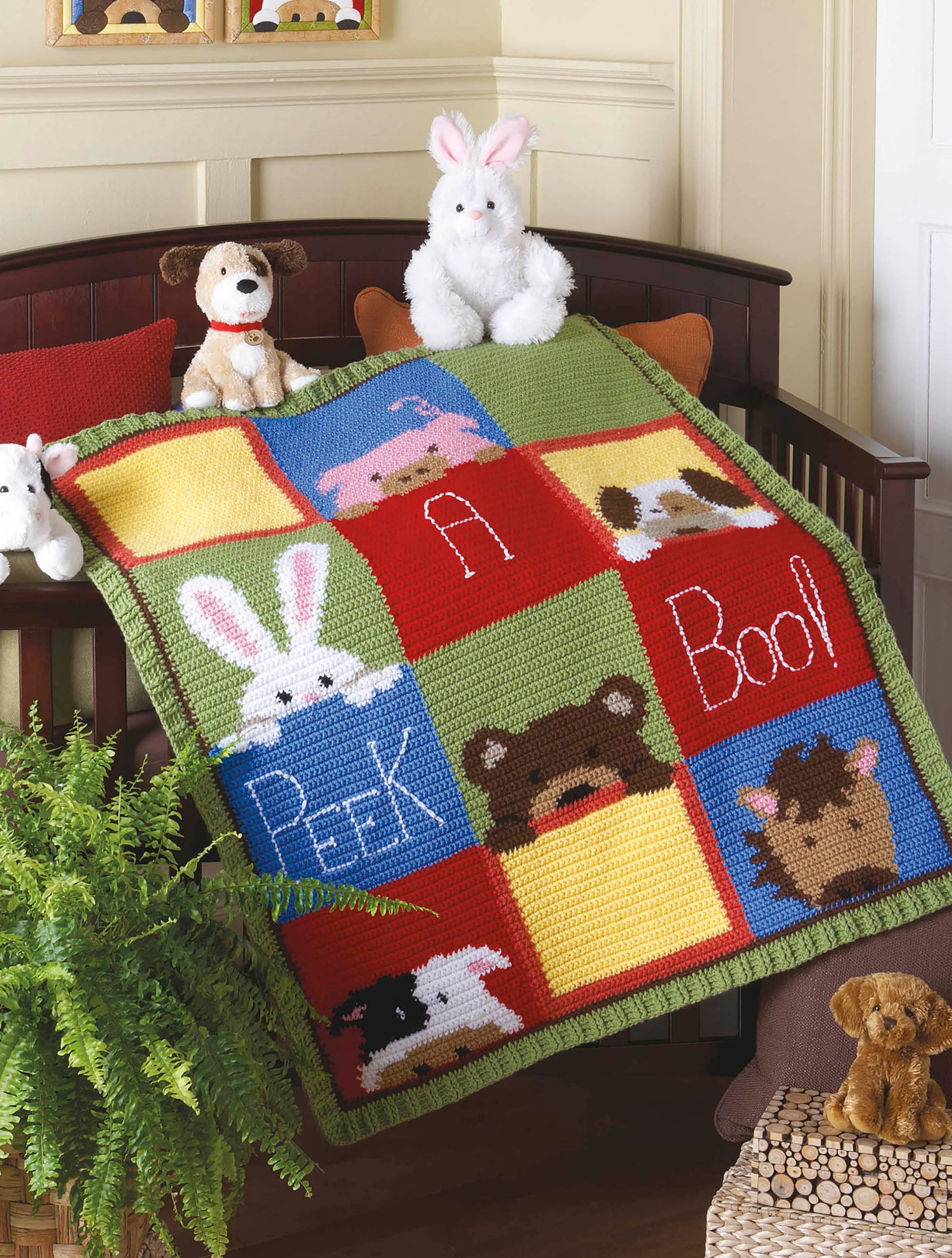 The Crochet Bedtime Blankies by Leisure Arts is a colorful crocheted baby blanket with cute cartoon animal faces, shown draped over a crib with plush stuffed animals and a green plant nearby.