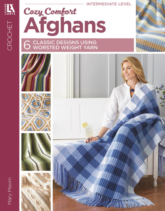 A woman smiles on a couch, wrapped in a blue and white checkered afghan. The book, Cozy Comfort Afghans by Leisure Arts, features six classic worsted weight designs; four crochet patterns are displayed on the left.