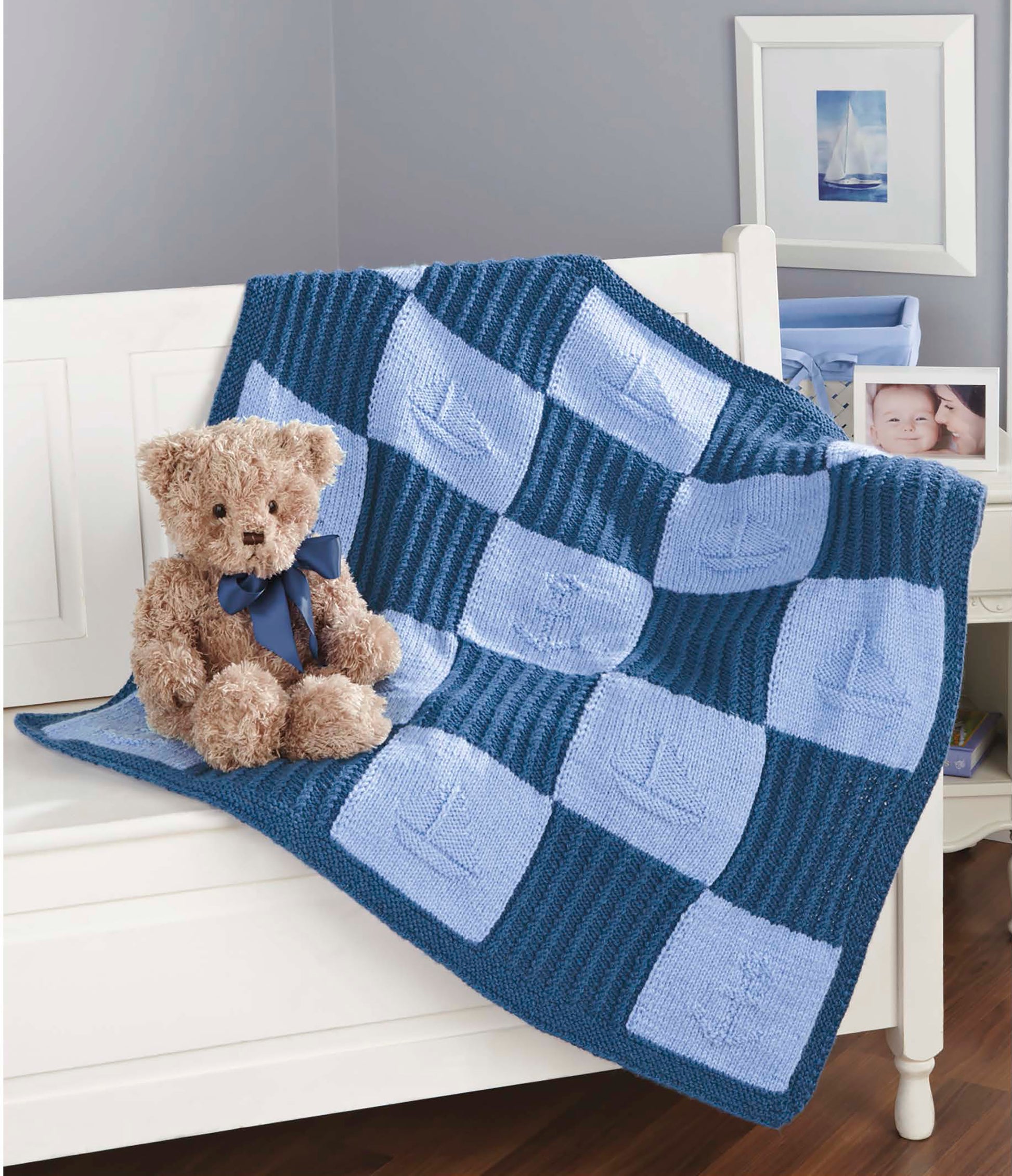 A plush teddy bear with a blue ribbon sits on a white bench draped with a blue patchwork sailboat blanket—just one of the charming projects in "Timeless Knit Baby Blankets" by Leisure Arts, ideal for intermediate knitters using various yarn weights.