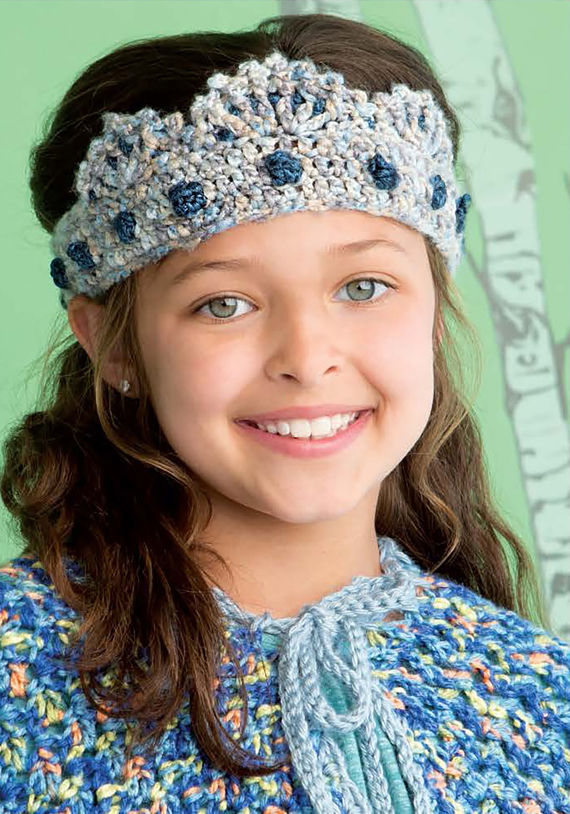 A smiling young girl with light eyes and brown hair wears a blue and gray crown headband from the Crochet Kids Dress Up Digital Download by Leisure Arts, standing before a green background with a tree illustration.