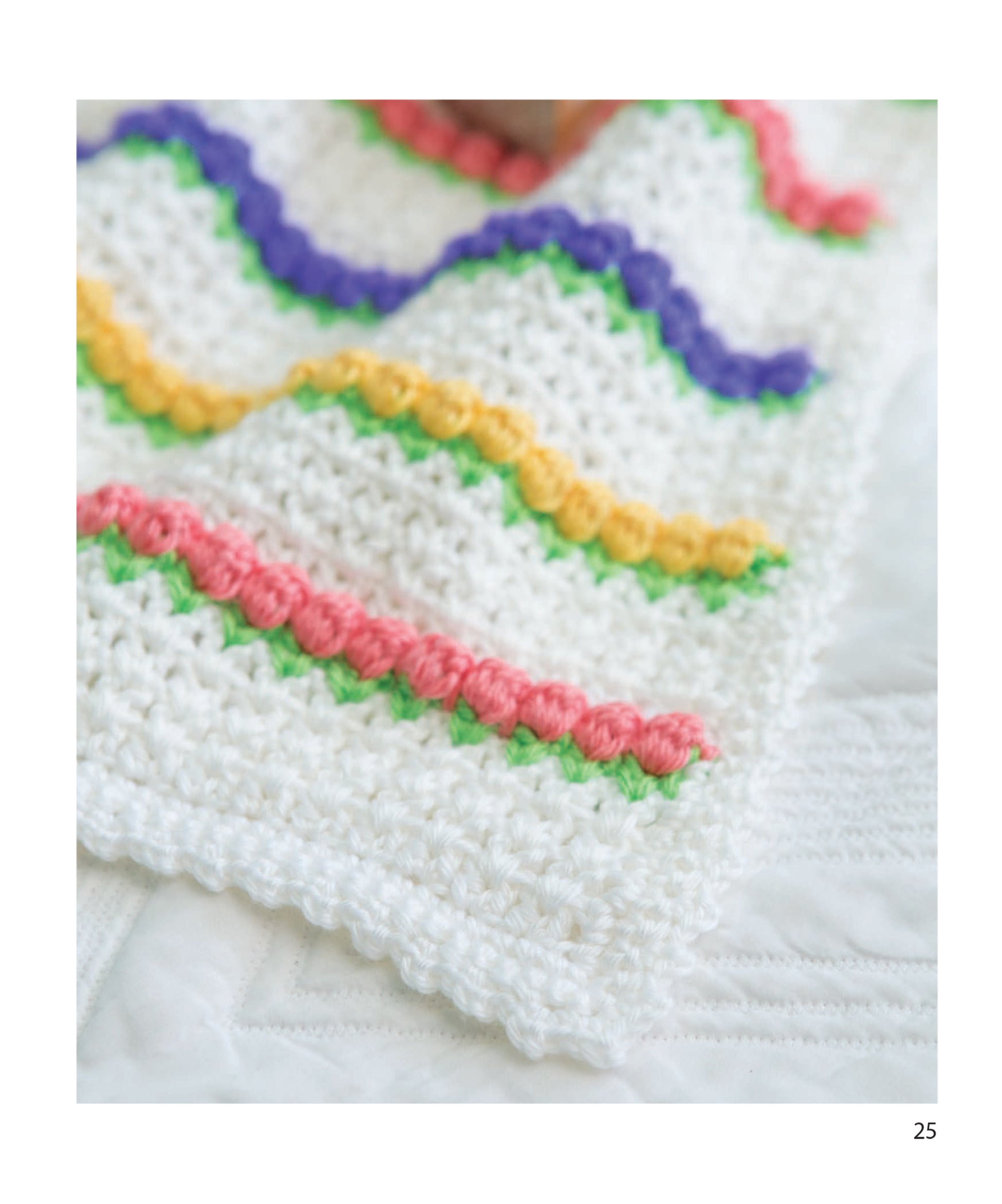 A close-up of the Leisure Arts Baby Bright Quilts displays beginner-friendly crochet patterns with colorful wavy rows in purple, yellow, pink, and green on a white quilted background.