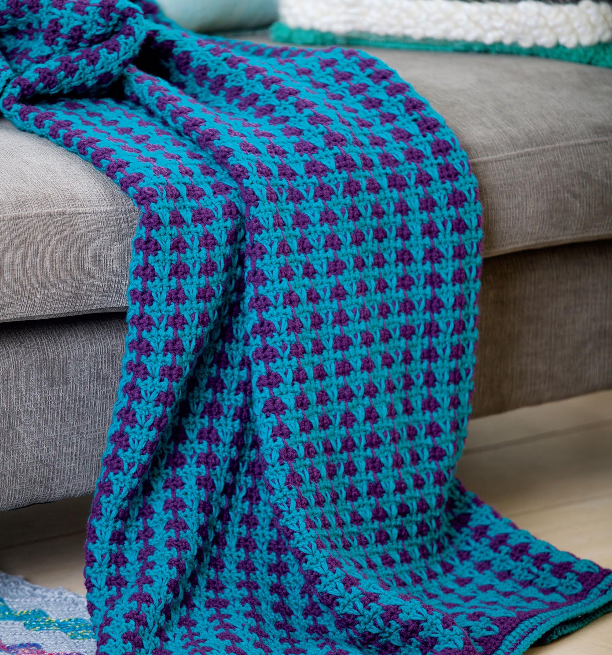 The "Afghans for the Family" pattern book by Leisure Arts features a blue and purple crocheted baby blanket with a textured checkerboard design—a cozy project perfect for your crochet collection.