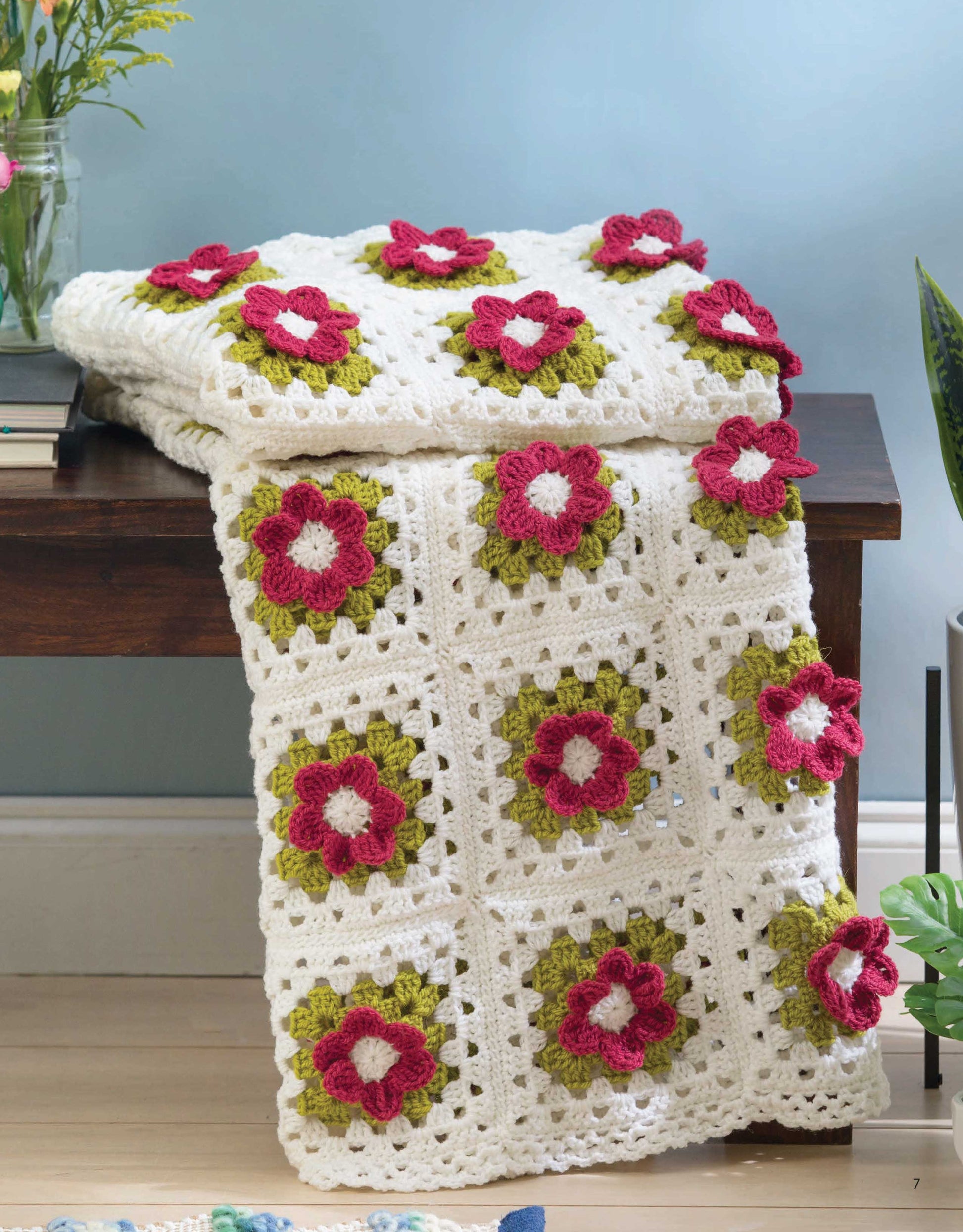 The Grannies In Bloom Digital Download by Leisure Arts features a crocheted blanket pattern with medium weight yarn and raised flower granny motifs in pink, red, and green on white squares—perfect for adding charm to any cozy space.