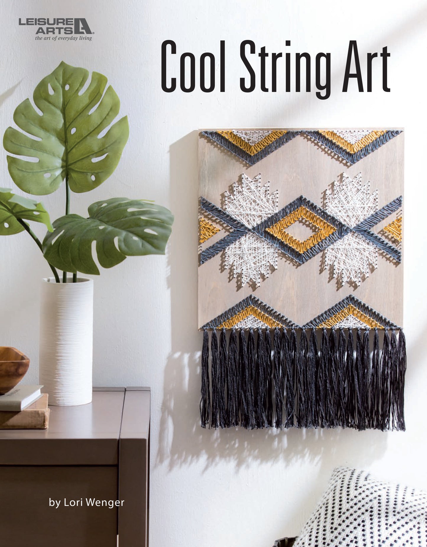 The cover of Cool String Art by Leisure Arts displays geometric string art made with gold, white, and black thread on a board, mounted above a wooden table with a white vase and plant.