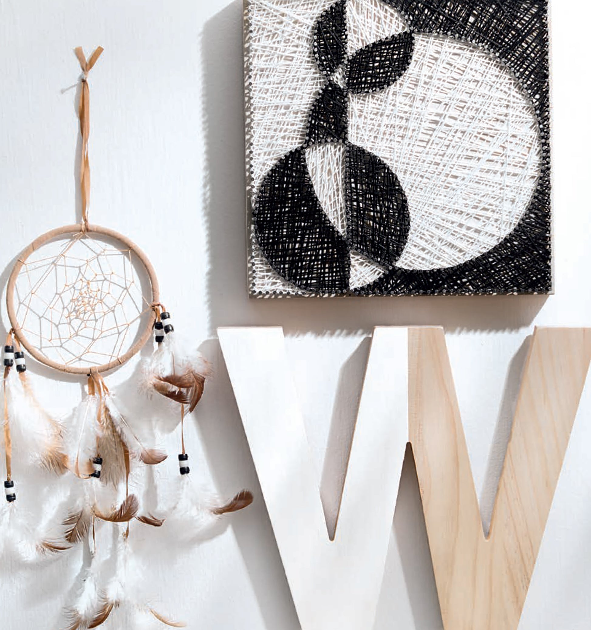 A beige dreamcatcher with feathers hangs on a white wall beside a large wooden W and the Leisure Arts Cool String Art, highlighting creative craft designs and unique DIY panel projects.