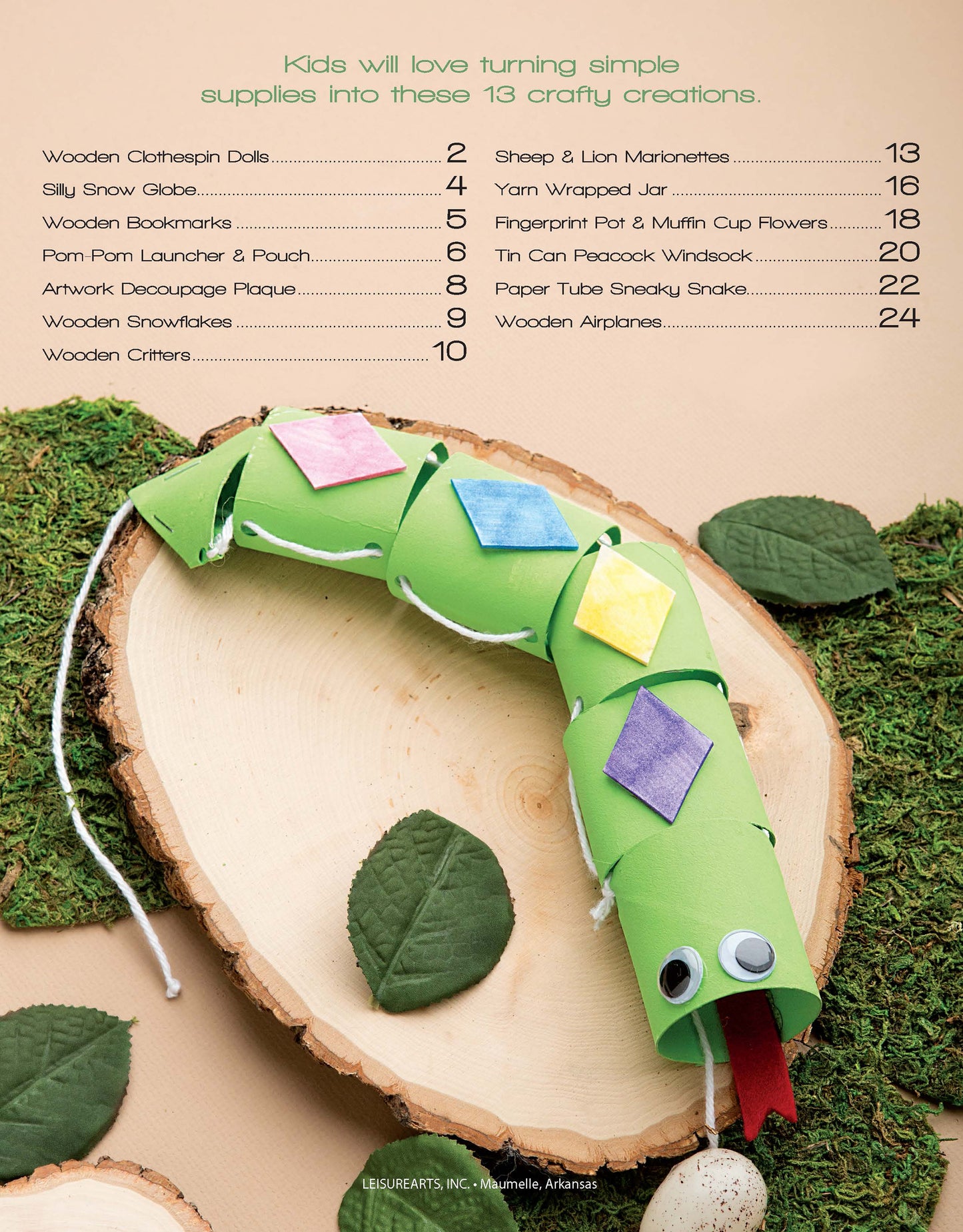 A green paper craft snake with colorful diamond shapes and googly eyes sits on a log amid artificial leaves and moss. DIY Simple Kids' Crafts by Leisure Arts is shown at the top, inspiring fun art activities for children.