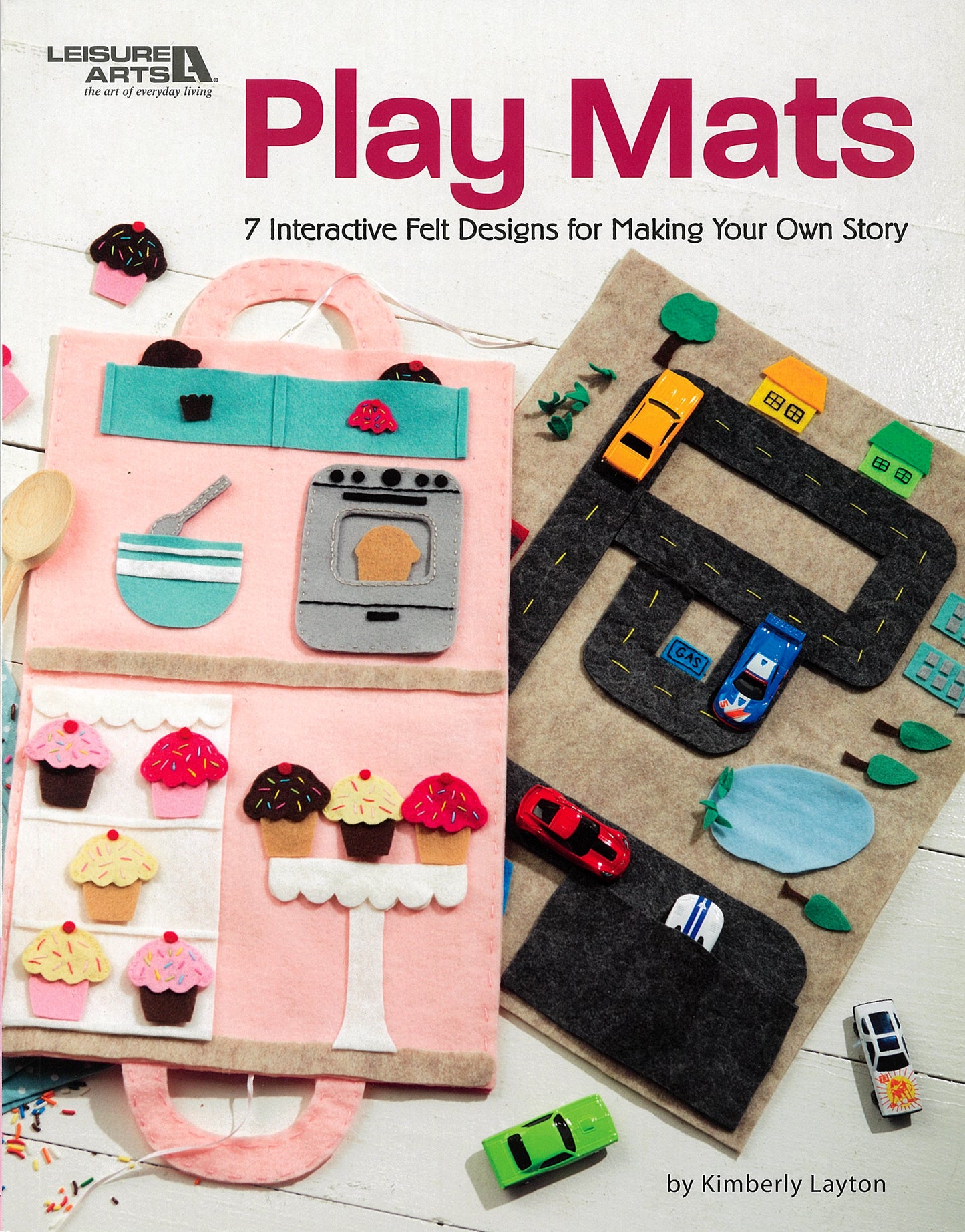 Cover of Play Mats—7 Interactive Felt Designs for Making Your Own Story by Leisure Arts, featuring felt play mats with kitchen, cupcake shop, and road layouts, plus toy cars. The subtitle highlights 7 interactive designs.