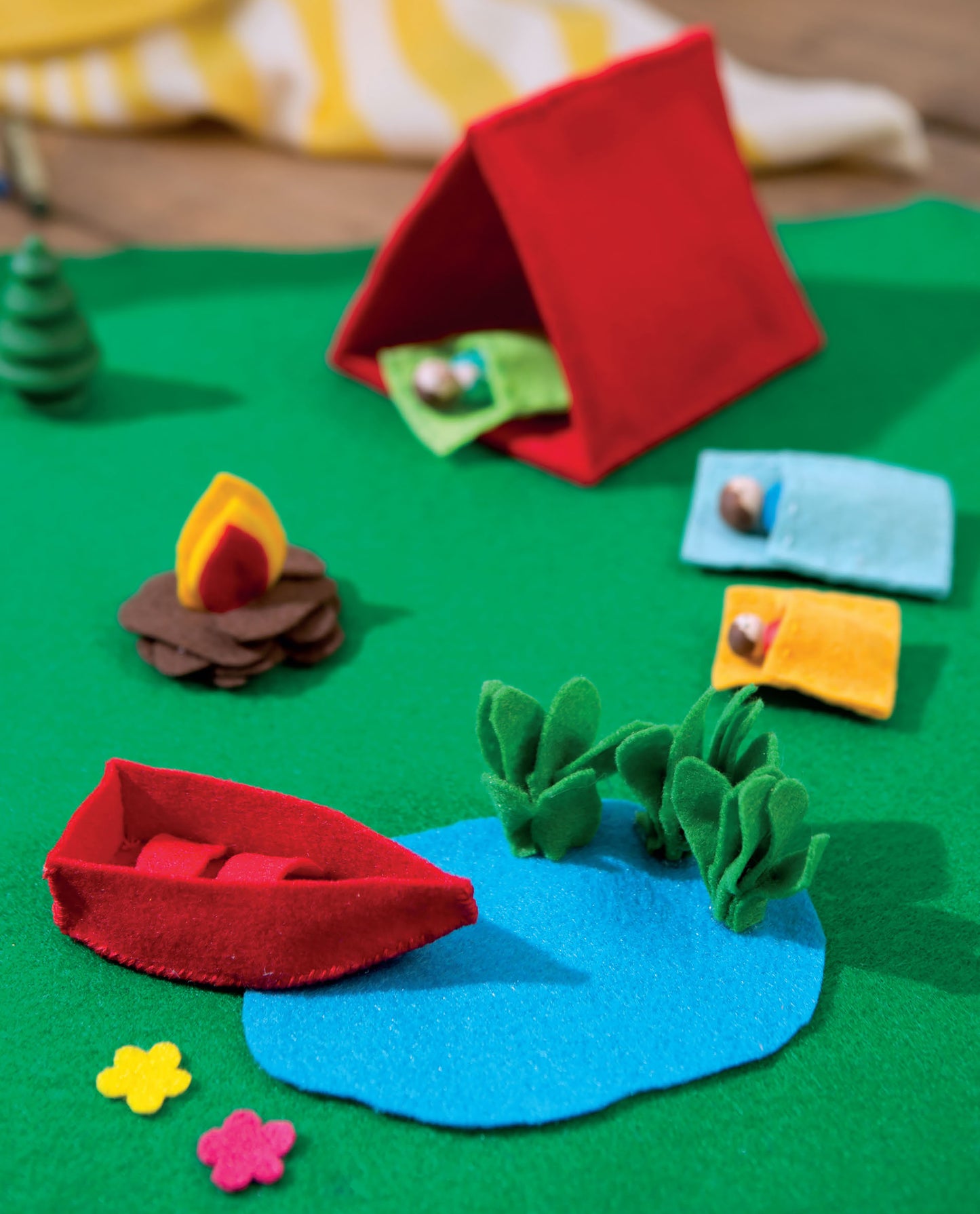 Leisure Arts Play Mats—7 Interactive Felt Designs let kids create stories with a colorful campsite scene, including a red tent, two sleeping bags, campfire, red canoe on blue pond, pine tree, bushes, and yellow flowers on grassy ground.