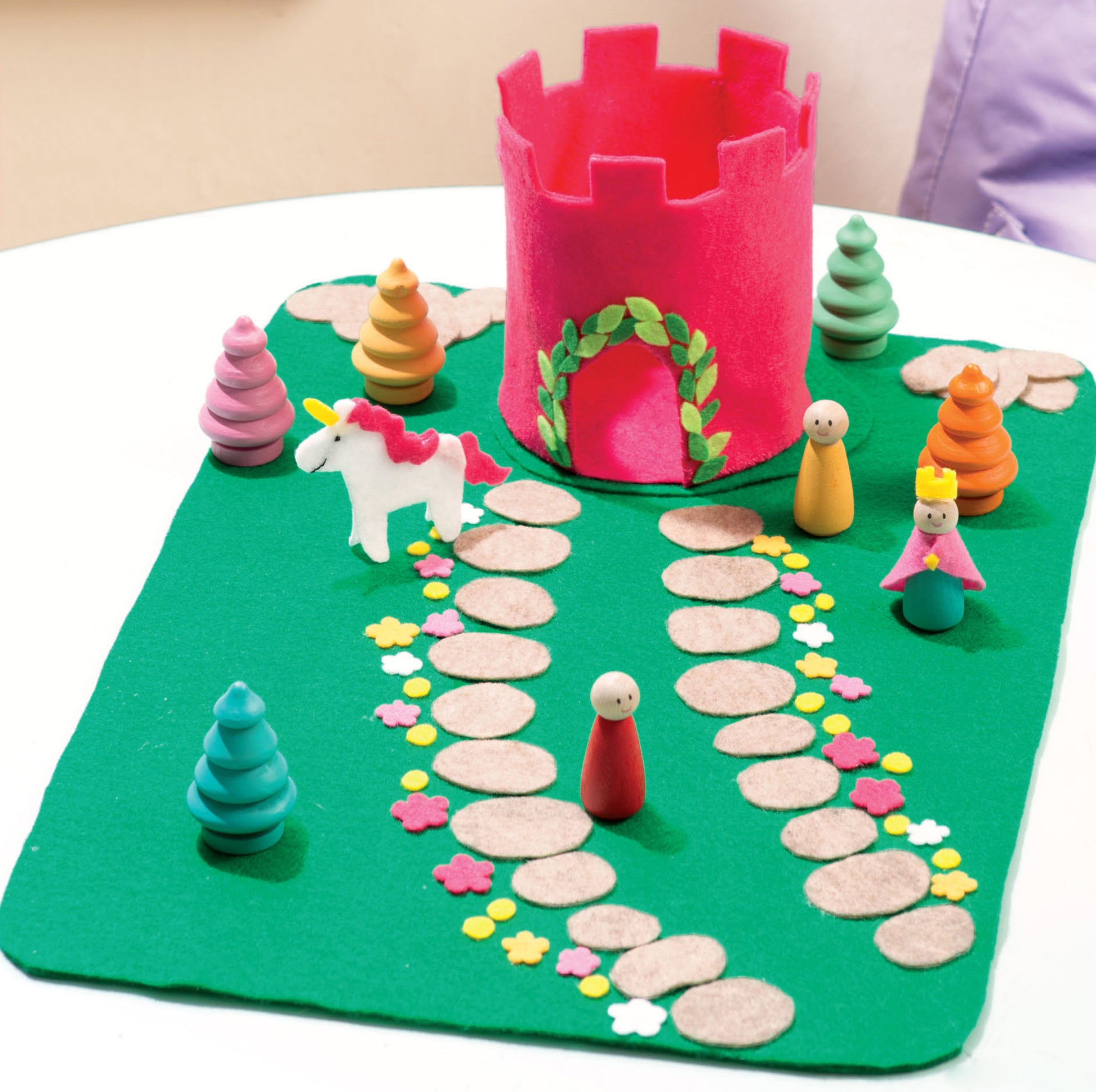 The Leisure Arts Play Mats feature 7 interactive felt designs, including stone paths, trees, peg people, a white unicorn with red mane, and a pink castle on green—perfect for creating your own story.