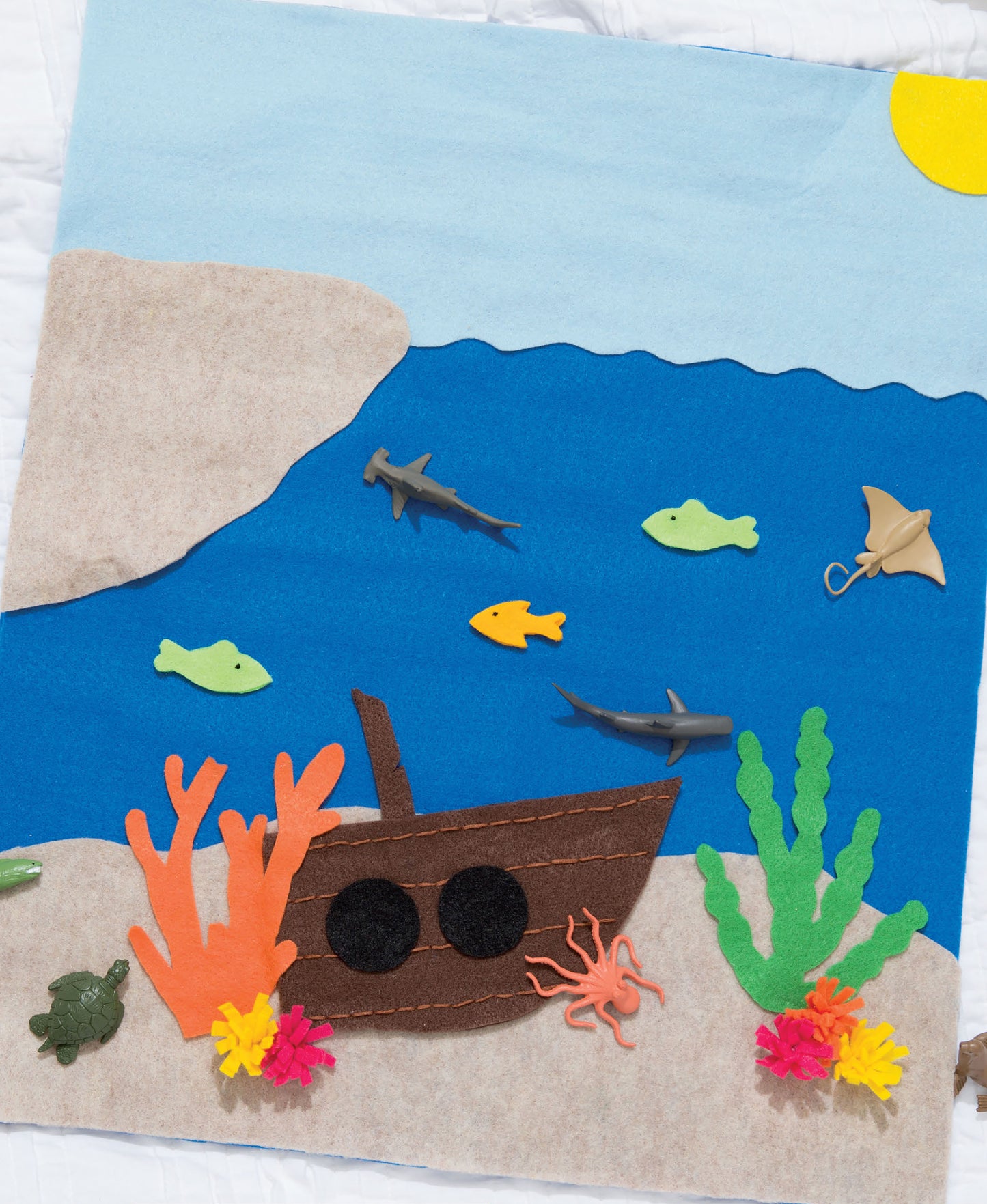 Create your own story with Leisure Arts Play Mats—featuring 7 interactive felt scenes, including an underwater world with a sunken ship, magical castle, sea creatures, colorful coral, and fish swimming under the sun.