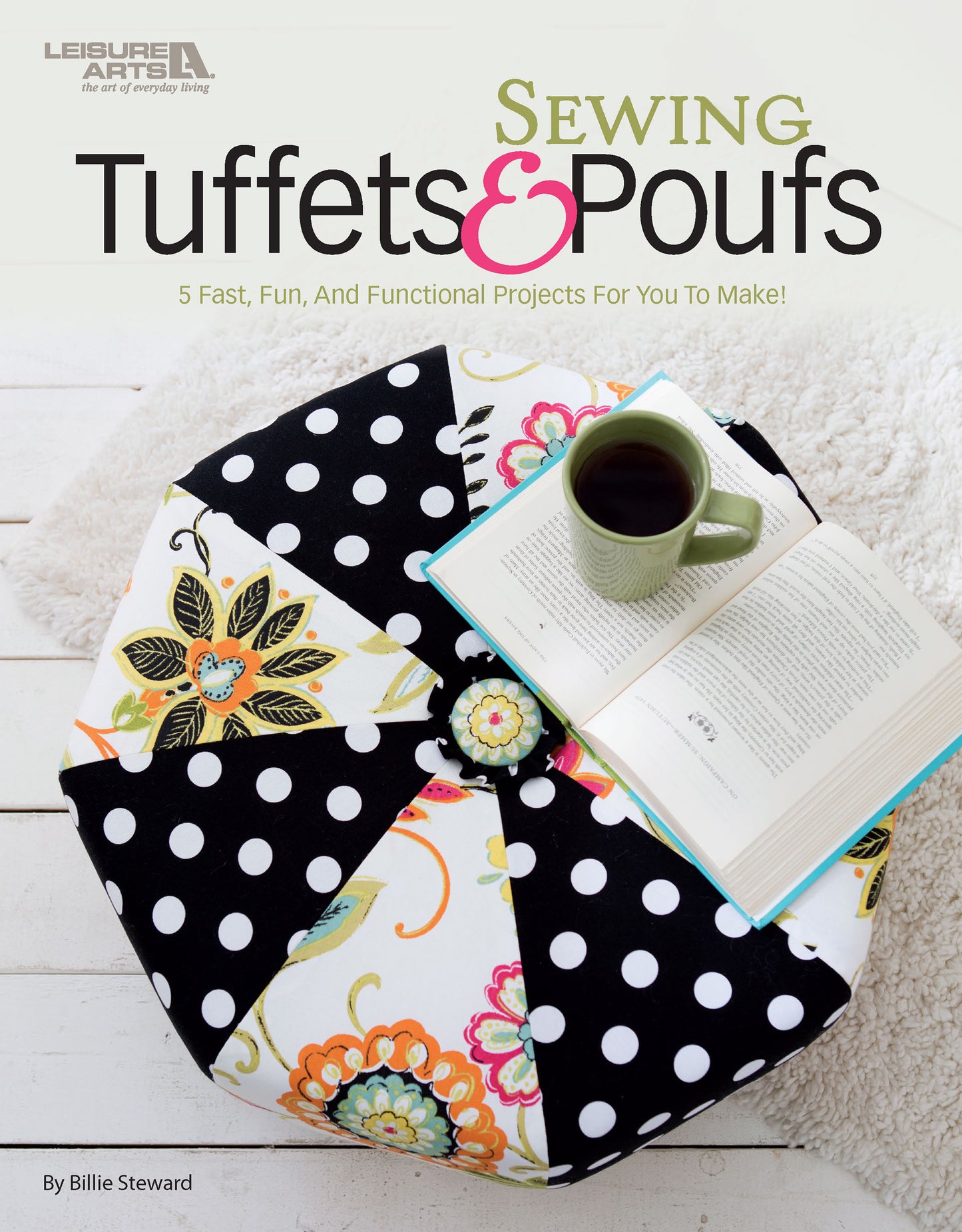 Leisure Arts' “Sewing Tuffets & Poufs” book rests on a vibrant pouf with black and white polka dots and floral patterns, alongside an open book and green mug, all placed on a white wooden floor.