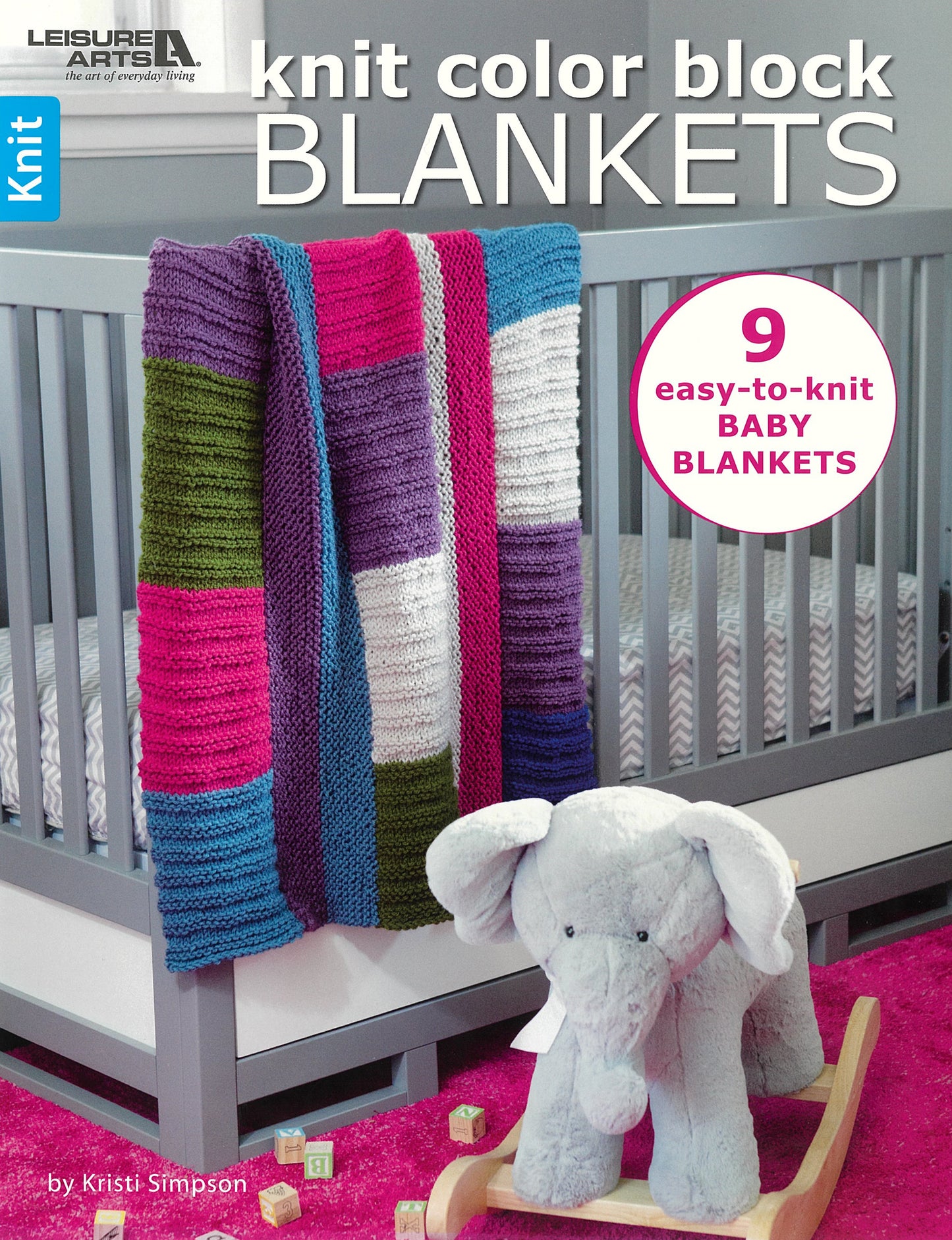 The Knit Color Block Blankets by Leisure Arts features a colorful baby blanket draped over a gray crib with a gray stuffed elephant nearby. Discover “9 easy knit baby blankets”—perfect beginner patterns by Kristi Simpson.