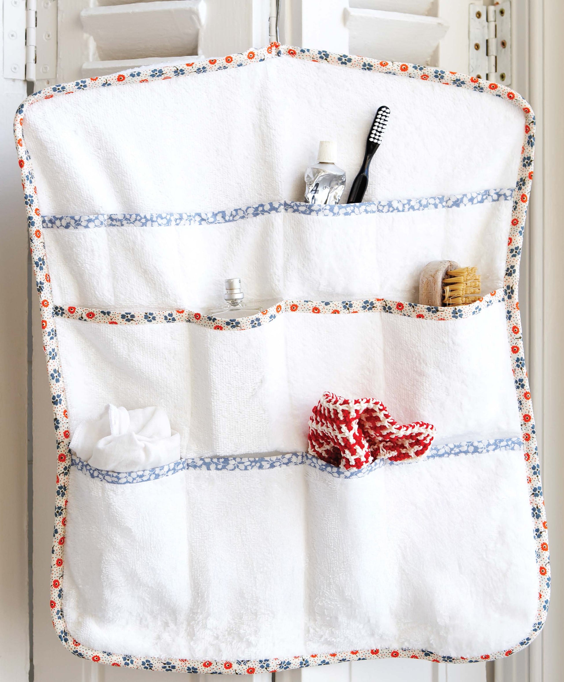 The Sewing Home kit by Leisure Arts offers an 11-project decor collection, including a white, sashiko-embroidered hanging organizer with seven floral-trimmed pockets—perfect on a door for toiletries and washcloths.