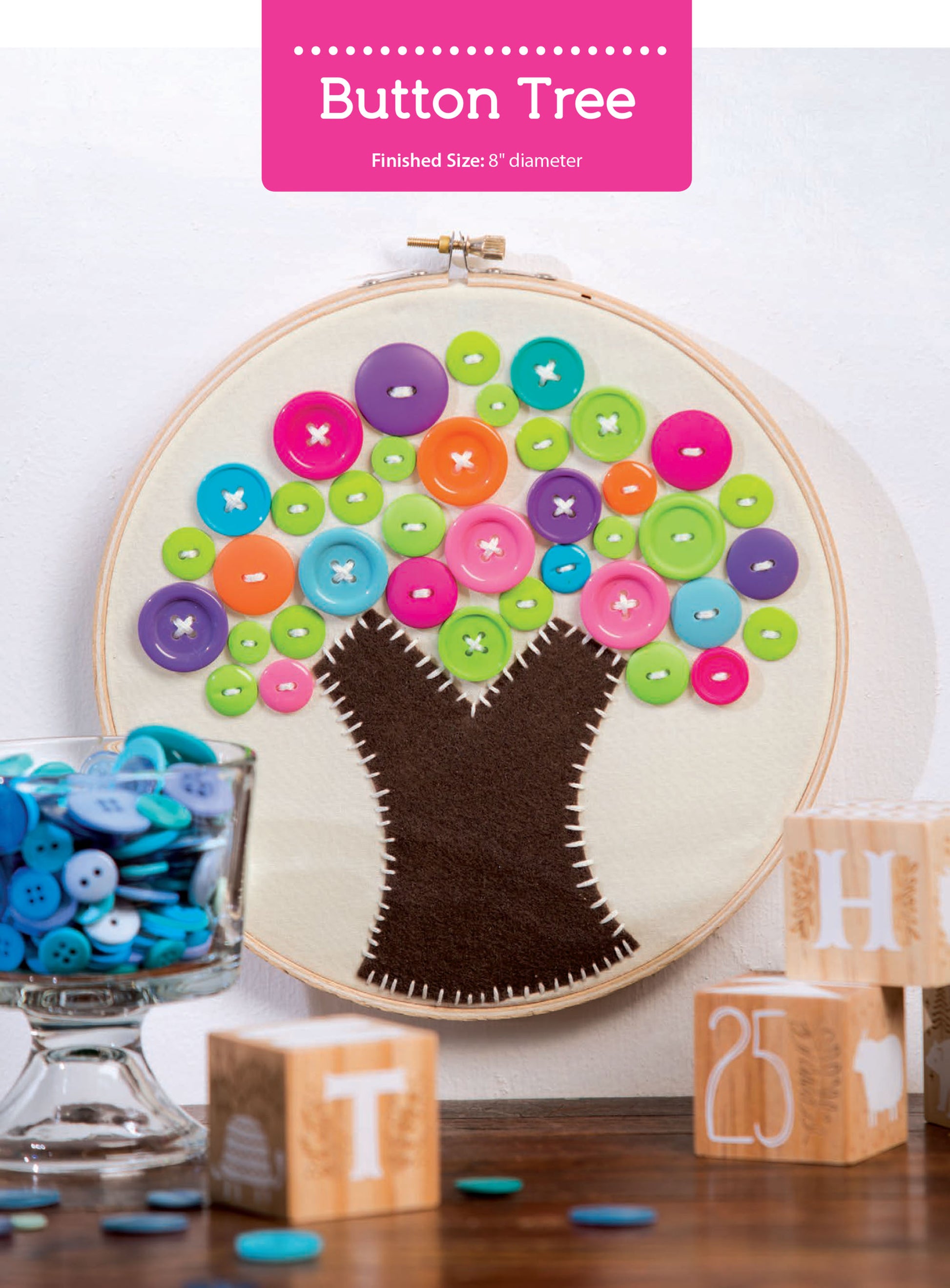 The After-School Kids' Crafts kit by Leisure Arts features a fabric tree with a brown felt trunk and colorful button leaves in an embroidery hoop, perfect for beginner craft ideas. It’s displayed with wooden blocks and a jar of blue buttons.