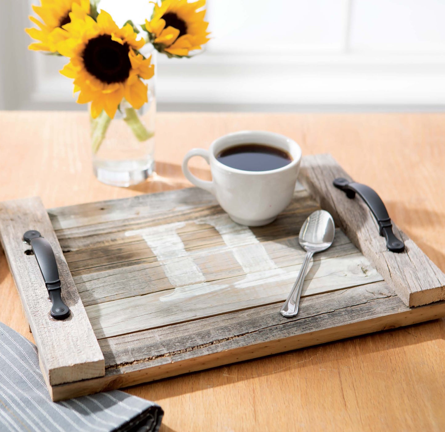 On a wooden table, the Do-It-Yourself Pallet Projects by Leisure Arts displays a rustic tray holding black coffee and a spoon, with a vase of sunflowers and folded striped napkin nearby.