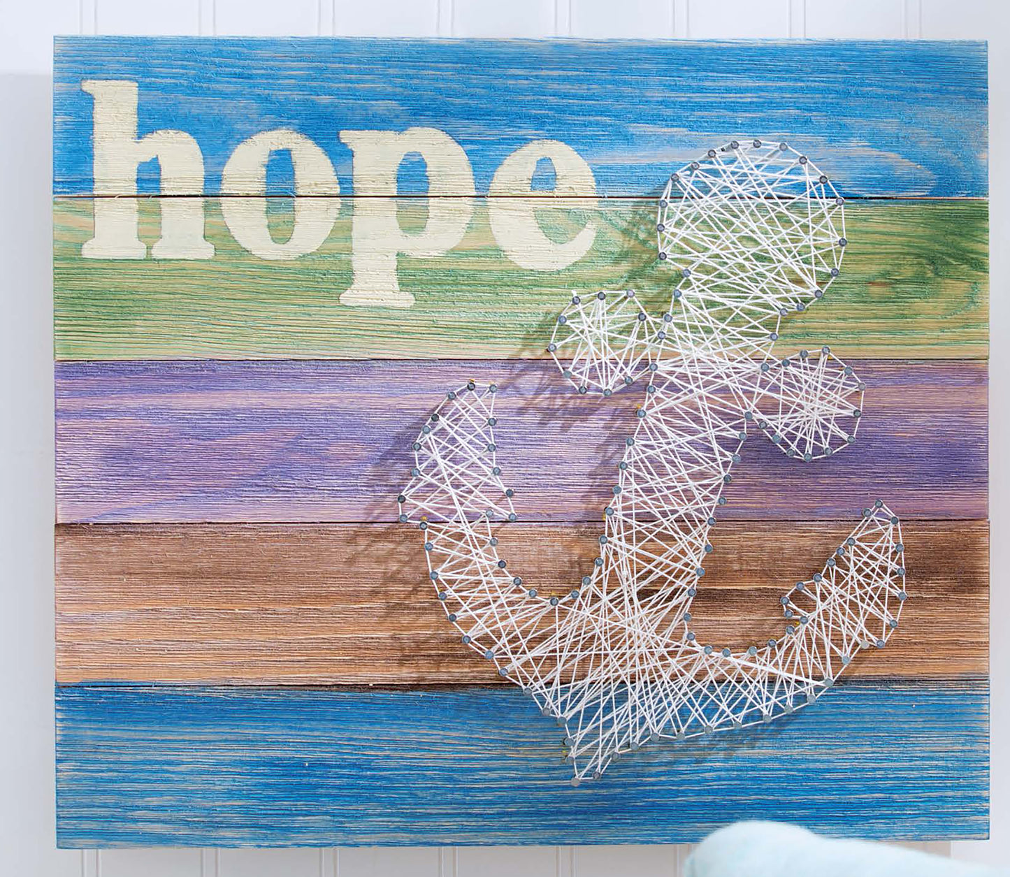 The “Do-It-Yourself Pallet Projects” book by Leisure Arts features a wooden sign from shipping pallets with pastel stripes and a white string art anchor and “hope”—a charming piece to enhance your DIY pallet crafts collection.