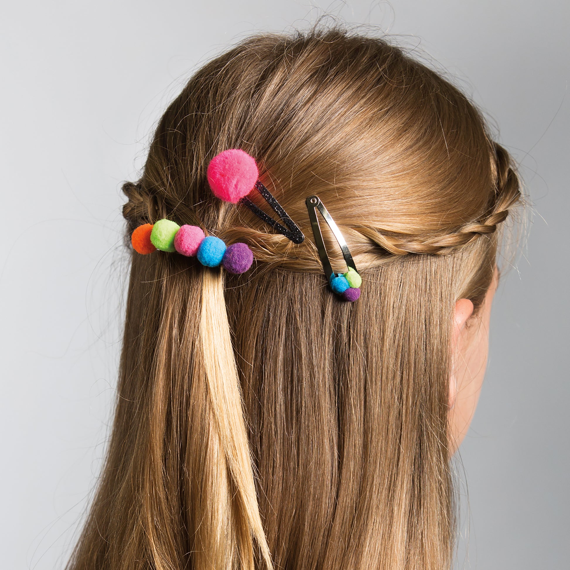A person with long, straight hair styled in a braid adorned with Leisure Arts Pom-Pom Crafts colorful hair clips—an ideal inspiration for easy pom-pom projects or beginner crafts. The photo is taken from behind against a neutral background.