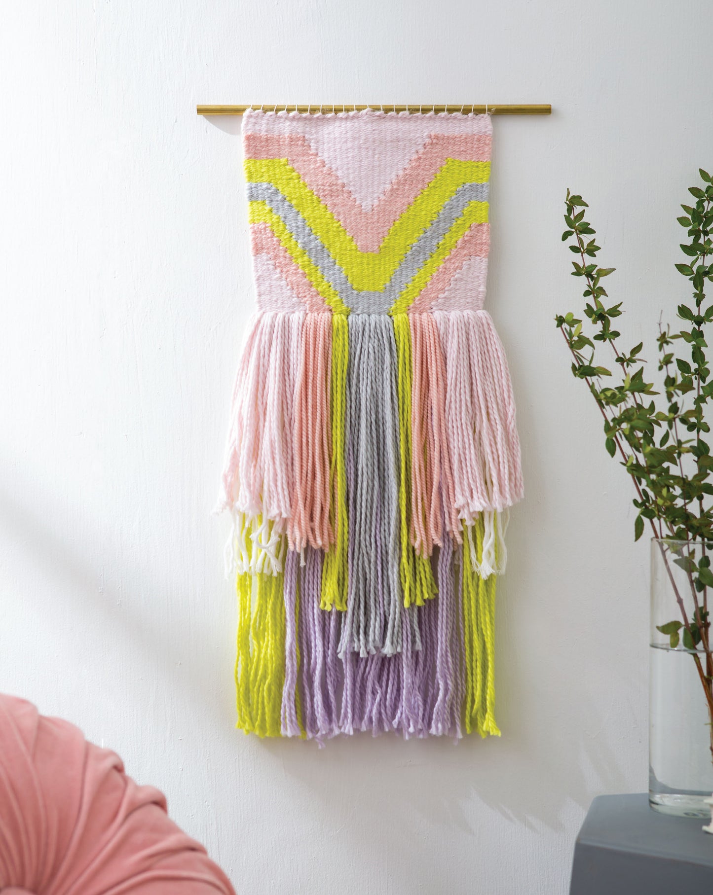 Create beautiful woven wall hangings with chevron patterns using the "Learn to Make Woven Wall Hangings" kit by Leisure Arts. Perfect for beginners, this kit features pastel pink, yellow, and gray yarns with long fringes and brass rod accents.