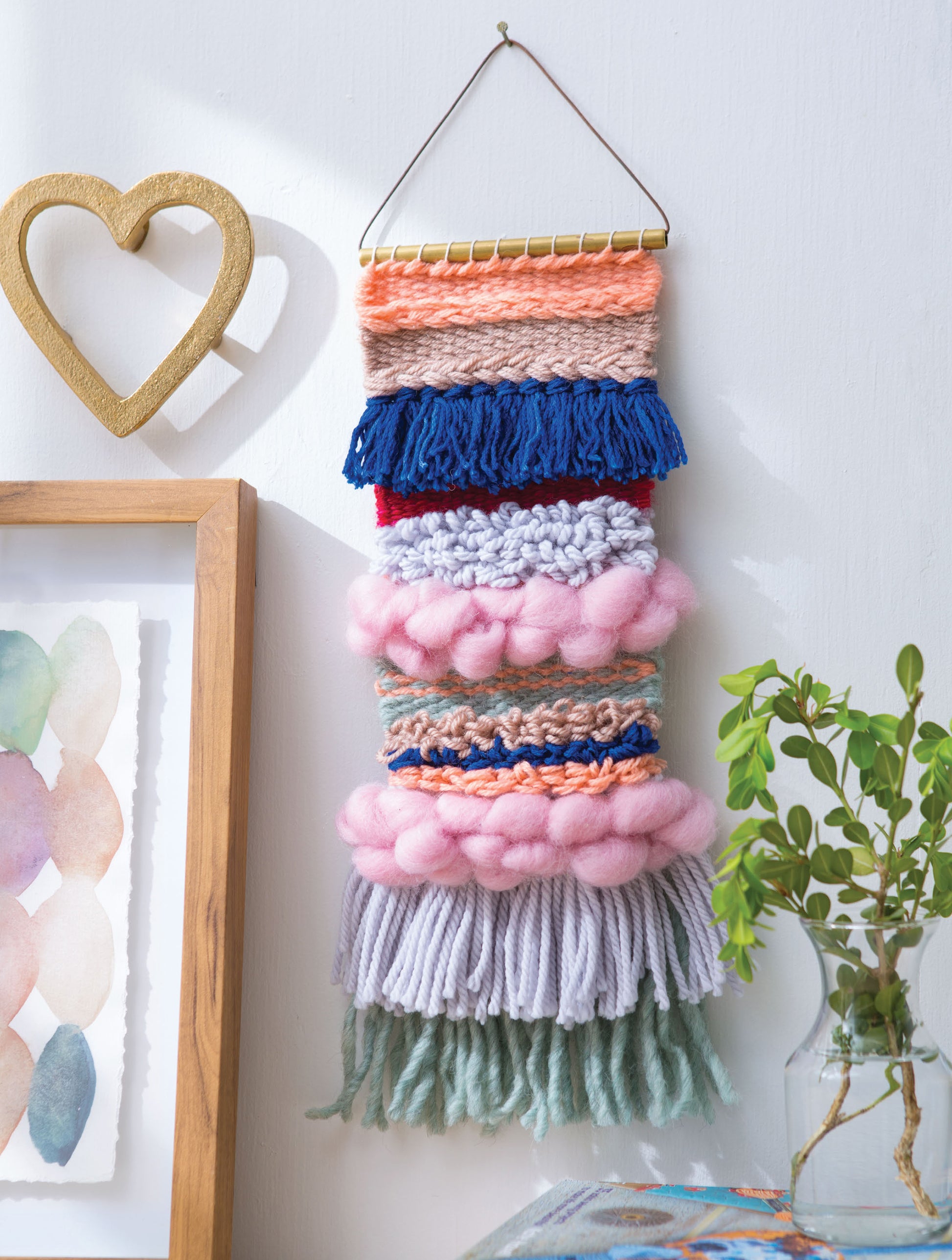 The "Learn to Make Woven Wall Hangings" by Leisure Arts features beginner tapestry patterns with colorful textured yarn in pink, blue, orange, and gray—great inspiration for frame loom projects and vibrant home décor.