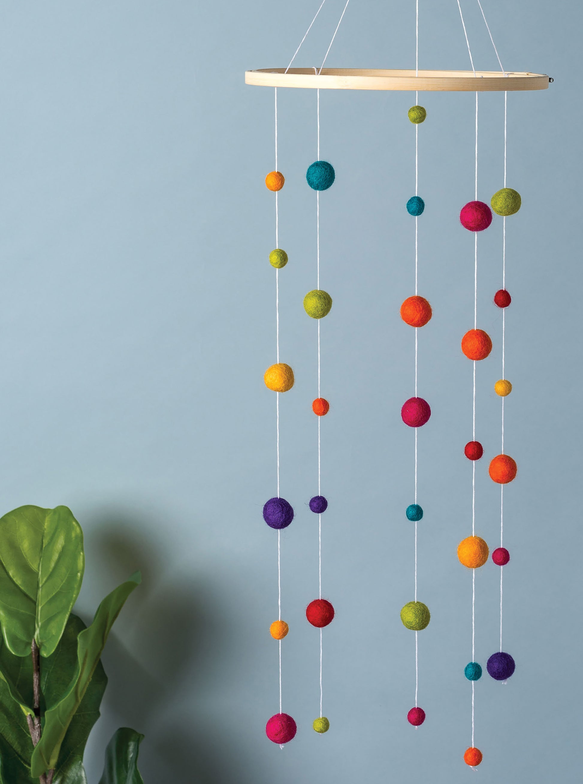 The Hoops Hooray! Digital Download by Leisure Arts features a hanging mobile crafted from colorful felt balls in various sizes, suspended on white strings from an embroidery hoop, with a leafy green plant and a light blue background.