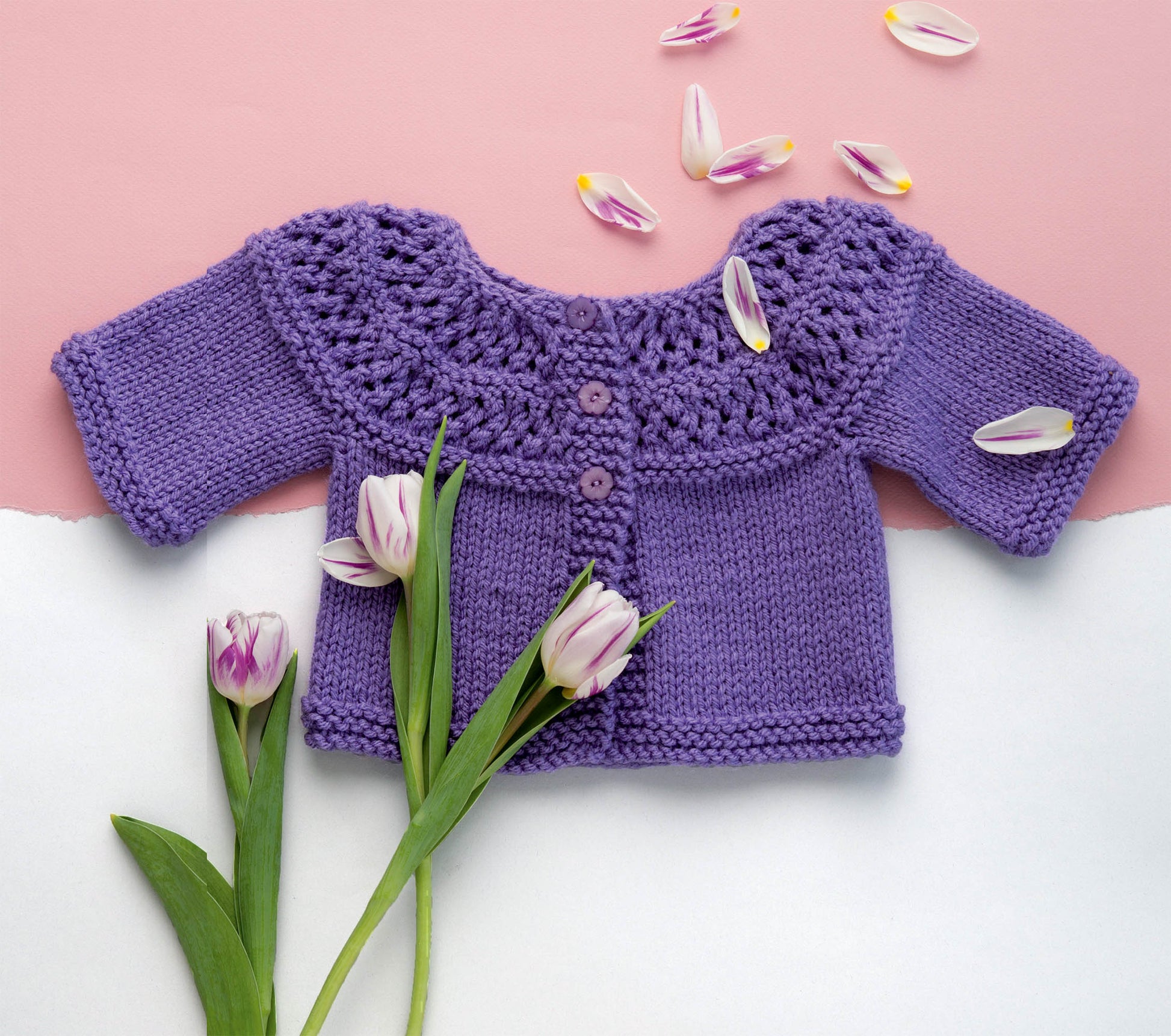The Adorable Baby Cardigans by Leisure Arts is a hand-knitted purple sweater made with worsted weight yarn, featuring three buttons. Displayed on a pink and white background with tulips, it's ideal for those seeking unique baby sweaters.