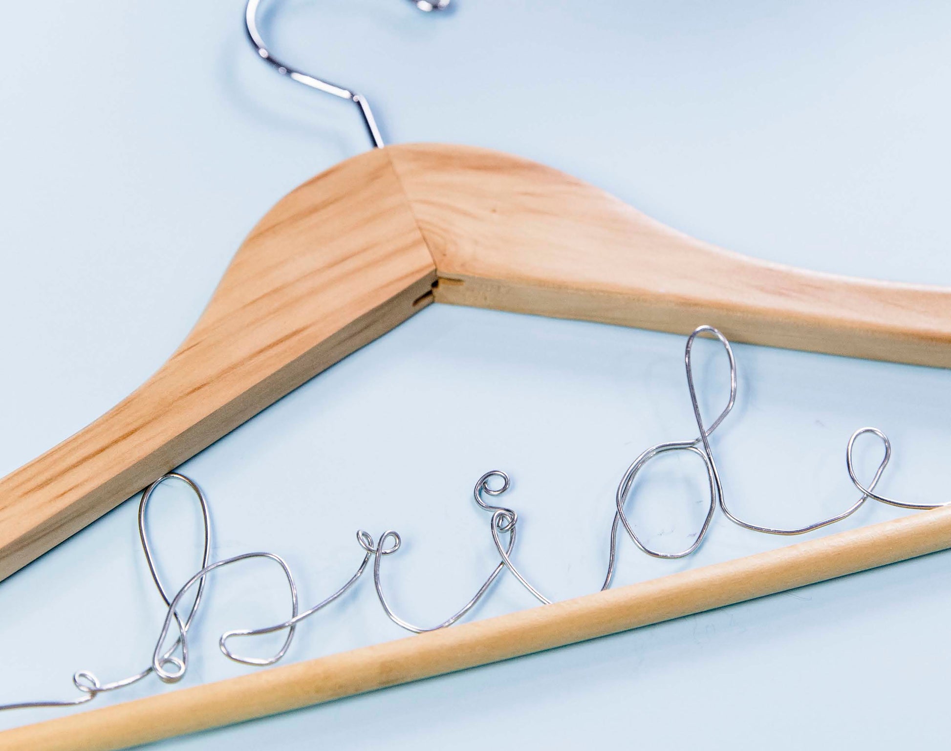 The Leisure Arts Handmade Wedding features a wooden clothes hanger with "bride" shaped from wire, set against a light blue background—ideal for personalized wedding décor and unique handmade crafts.
