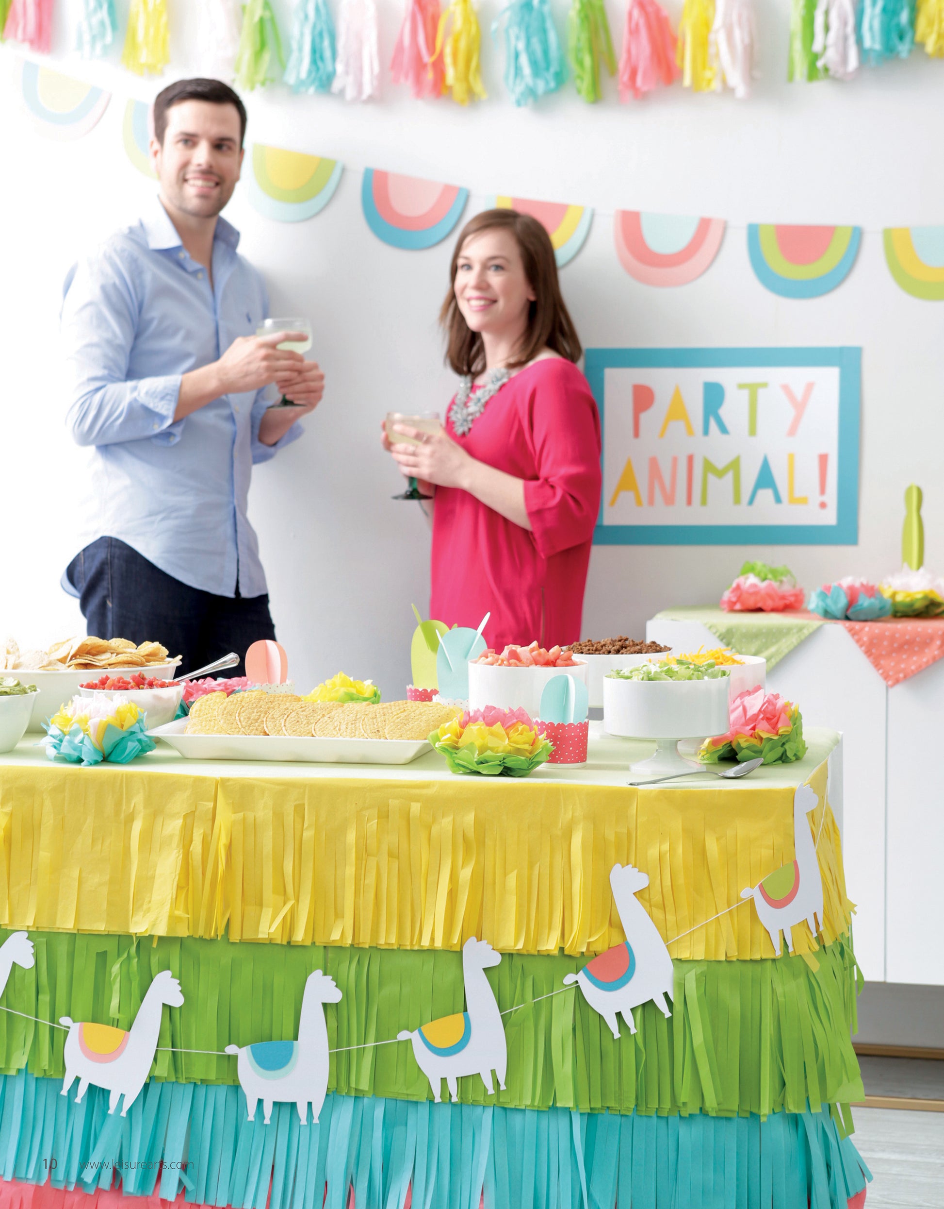 A man and woman enjoy drinks at a festive party decorated with projects from Leisure Arts’ Paper Party—Easy-to-Make Projects for Parties, Celebrations & Even Home Decor, featuring colorful fringe, llama accents, and vibrant “Party Animal!” décor.