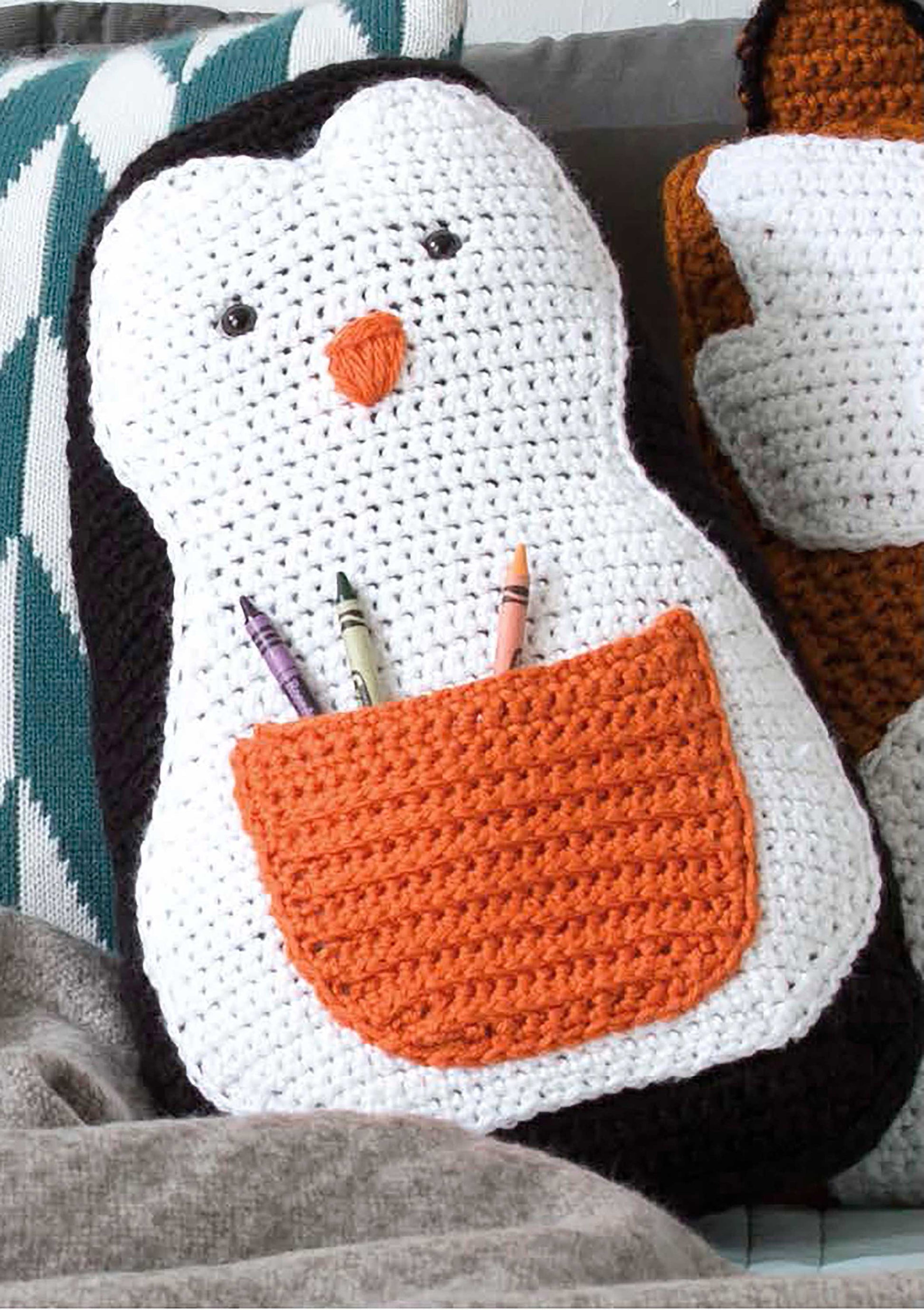 Leisure Arts’ Fun Animal Pillows—9 Huggable Friends to Stitch for Little Ones features adorable crochet designs like a penguin with a white face, black outline, orange beak, and crayon pocket—perfect for animal-shaped pillow fans.