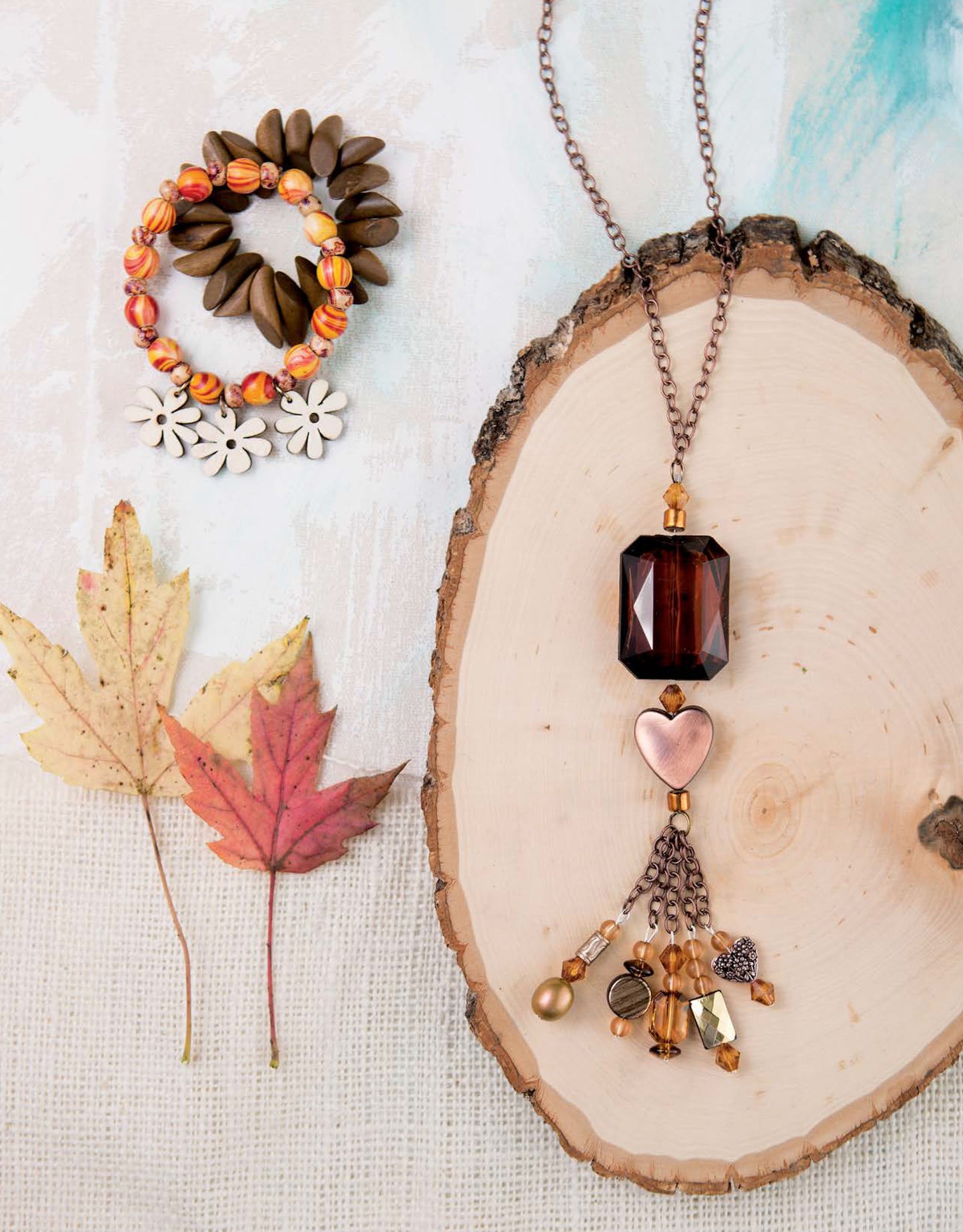 The Get Started in Jewelry Making Digital Download by Leisure Arts features a necklace with a dark brown pendant, dangling charms, and beaded bracelets—perfect inspiration for beginner jewelry projects. Autumn leaves add a seasonal touch.