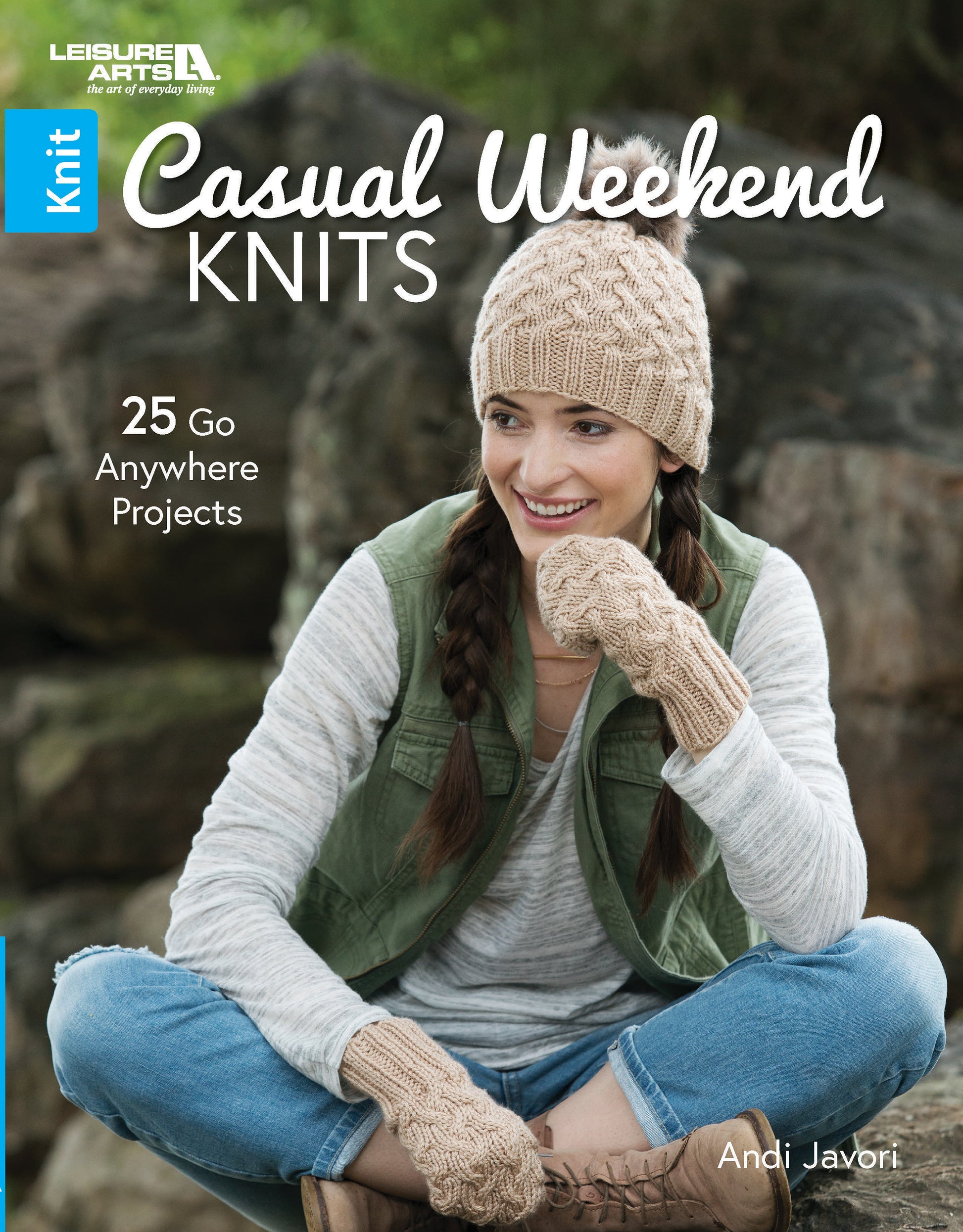 A woman sits on rocks outdoors, smiling in a knitted hat and fingerless gloves, beside "Casual Weekend Knits" by Leisure Arts—a book featuring 25 stylish, go-anywhere knitting patterns.