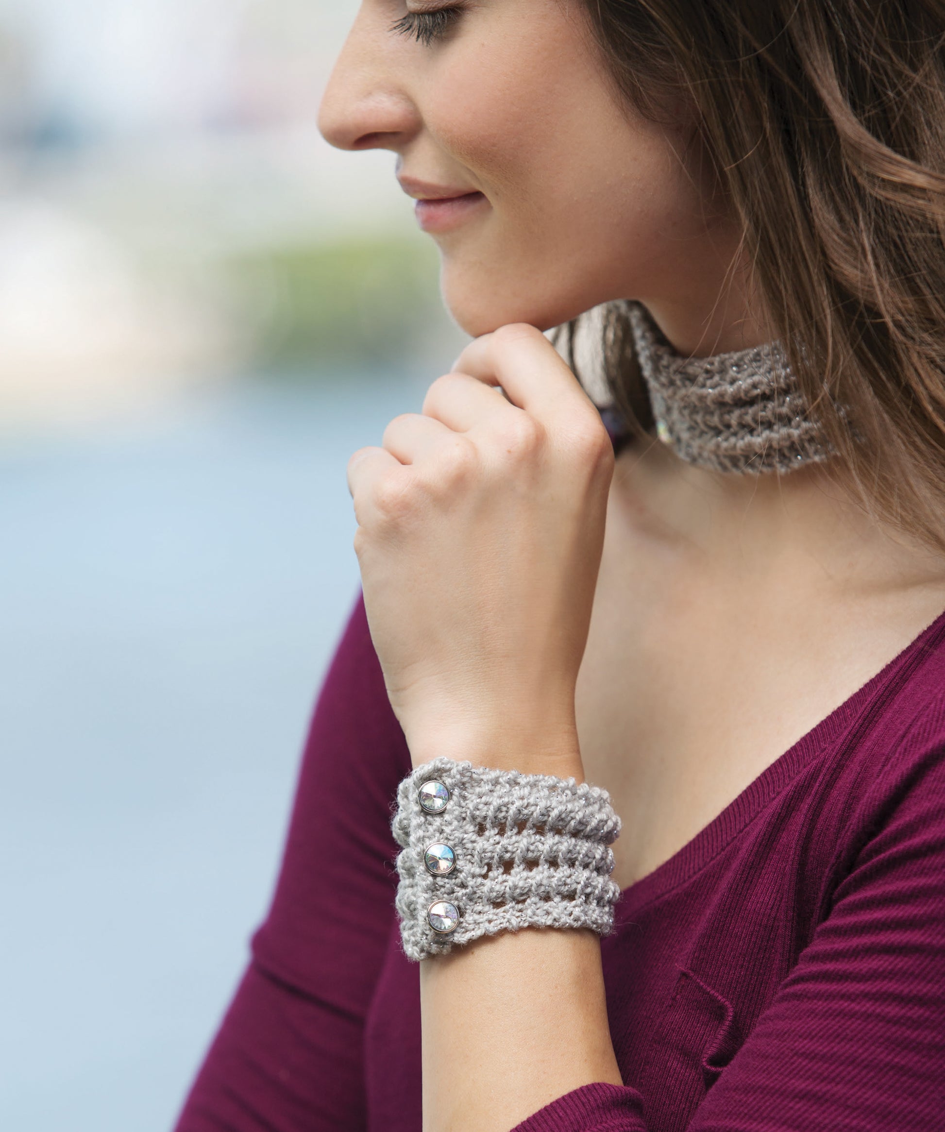 A woman in a burgundy top models a crocheted gray choker and matching wrist cuff with silver buttons—perfect inspiration from Casual Weekend Knits by Leisure Arts for wearable, creative knitting projects.
