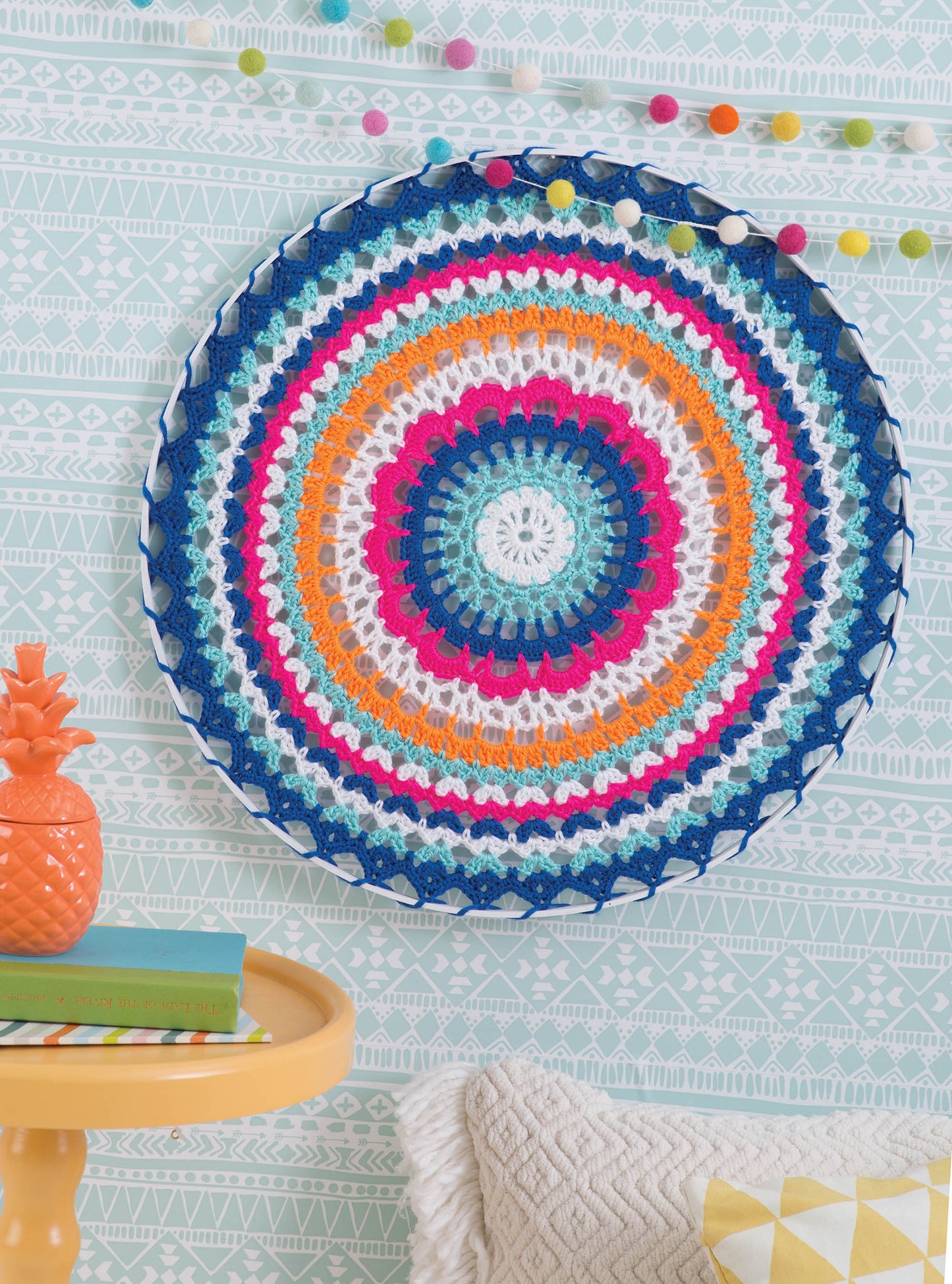 The book "Happy Crochet—13 Fun Projects That Are Sure to Brighten Your Day" by Leisure Arts features easy crochet patterns to make colorful mandala wall hangings in blue, orange, pink, white, and teal for cheerful home decor.