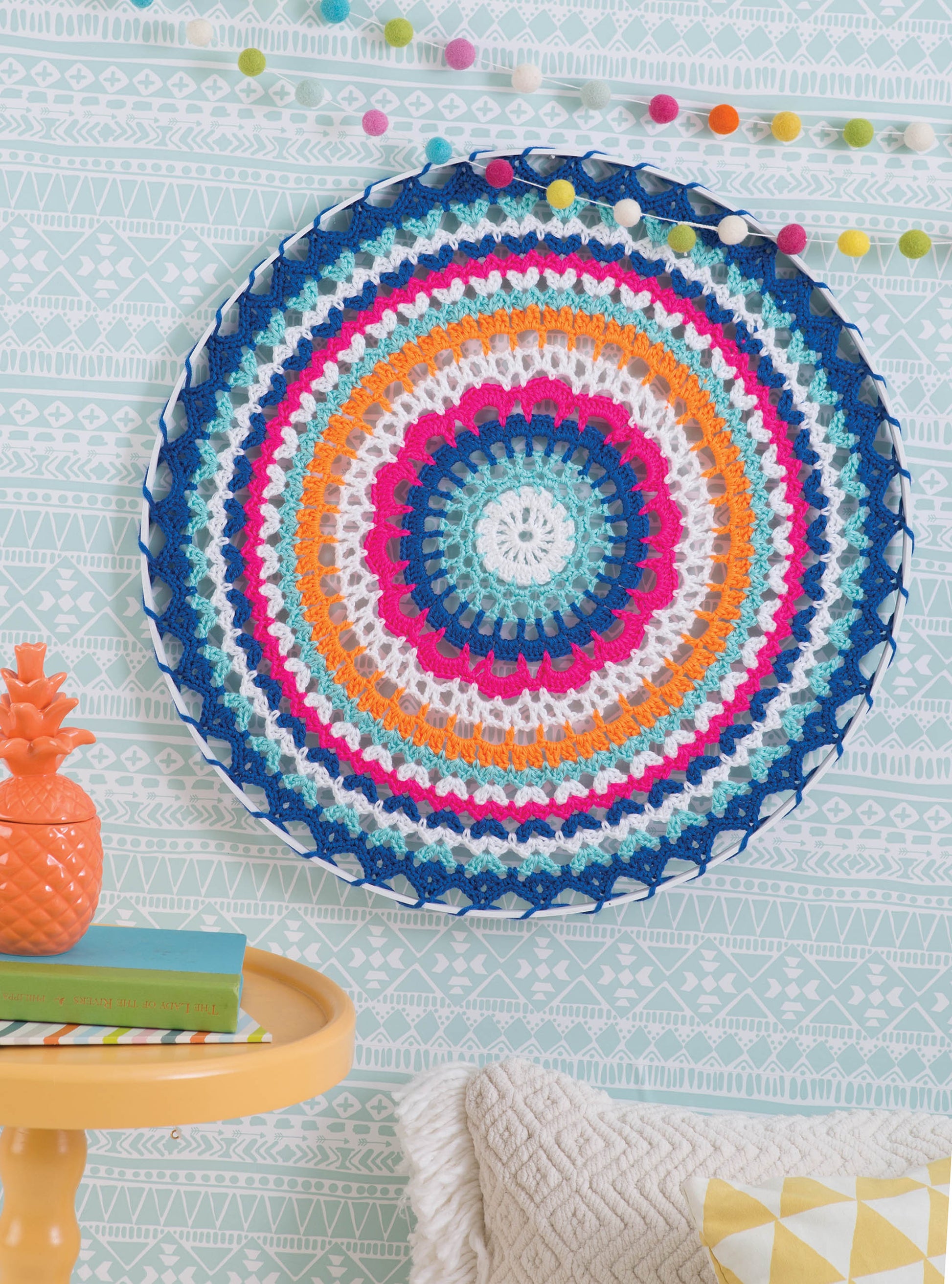 The book "Happy Crochet—13 Fun Projects That Are Sure to Brighten Your Day" by Leisure Arts features easy crochet patterns to make colorful mandala wall hangings in blue, orange, pink, white, and teal for cheerful home decor.