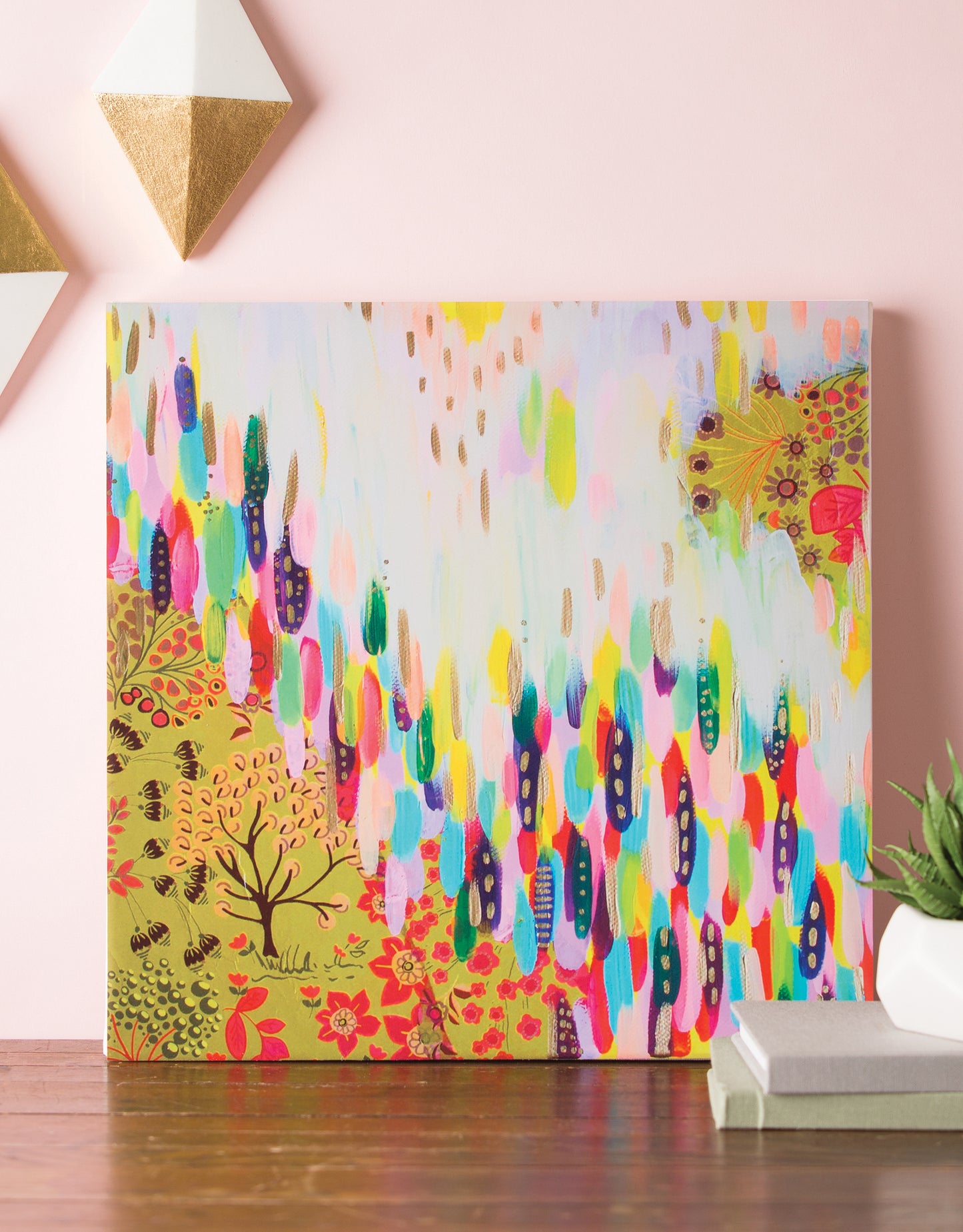 Happy Abstracts—Fearless Painting for True Beginners by Leisure Arts is displayed with colorful brushstrokes and floral, tree motifs on a wooden surface against a pale pink wall, complemented by geometric decor and a small plant.