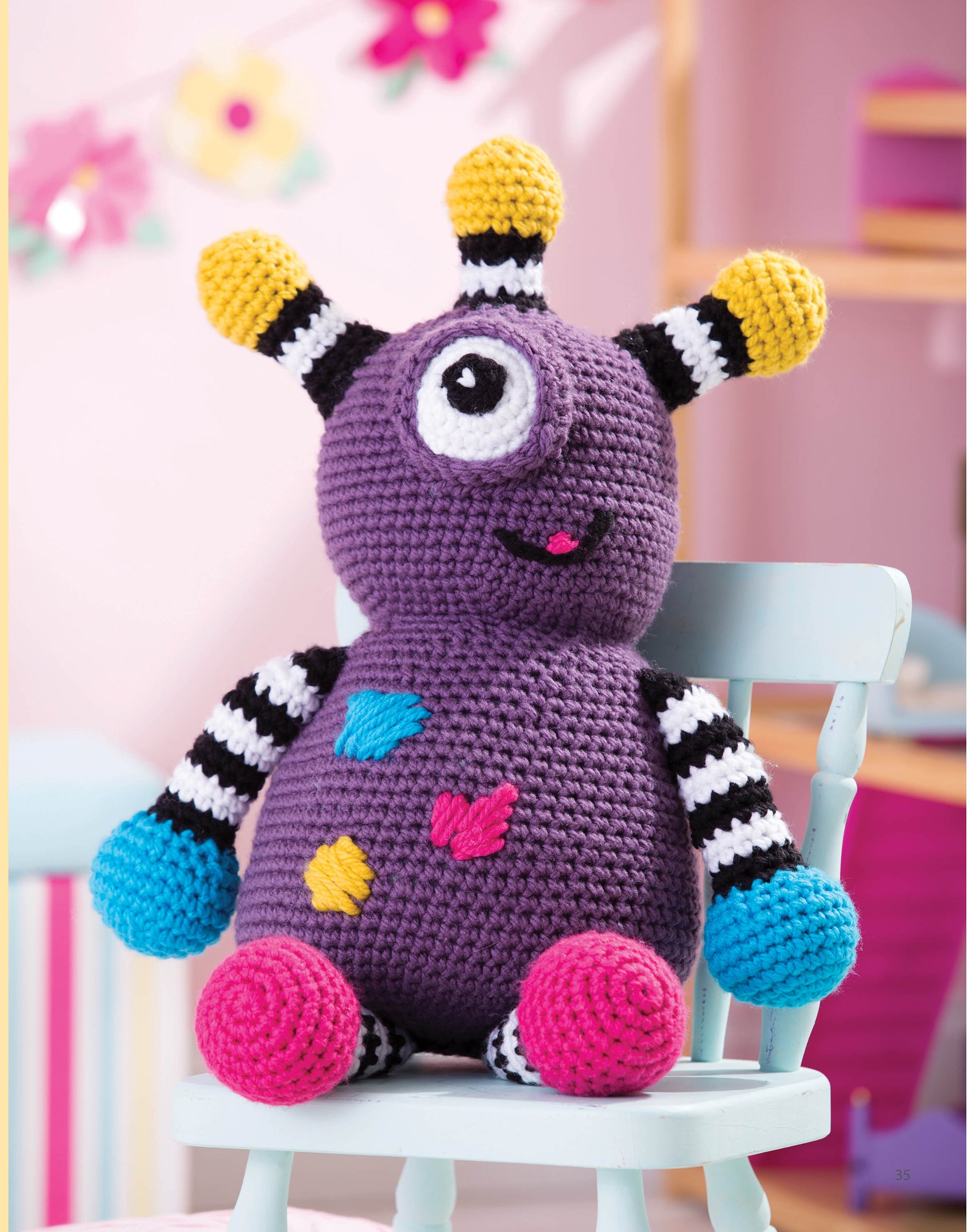 Leisure Arts’ Huggable Monsters: a crocheted purple toy with one big eye, colorful spots, striped arms, blue hands, and four yellow-tipped antennae—ideal for monster fans or beginner crochet projects.
