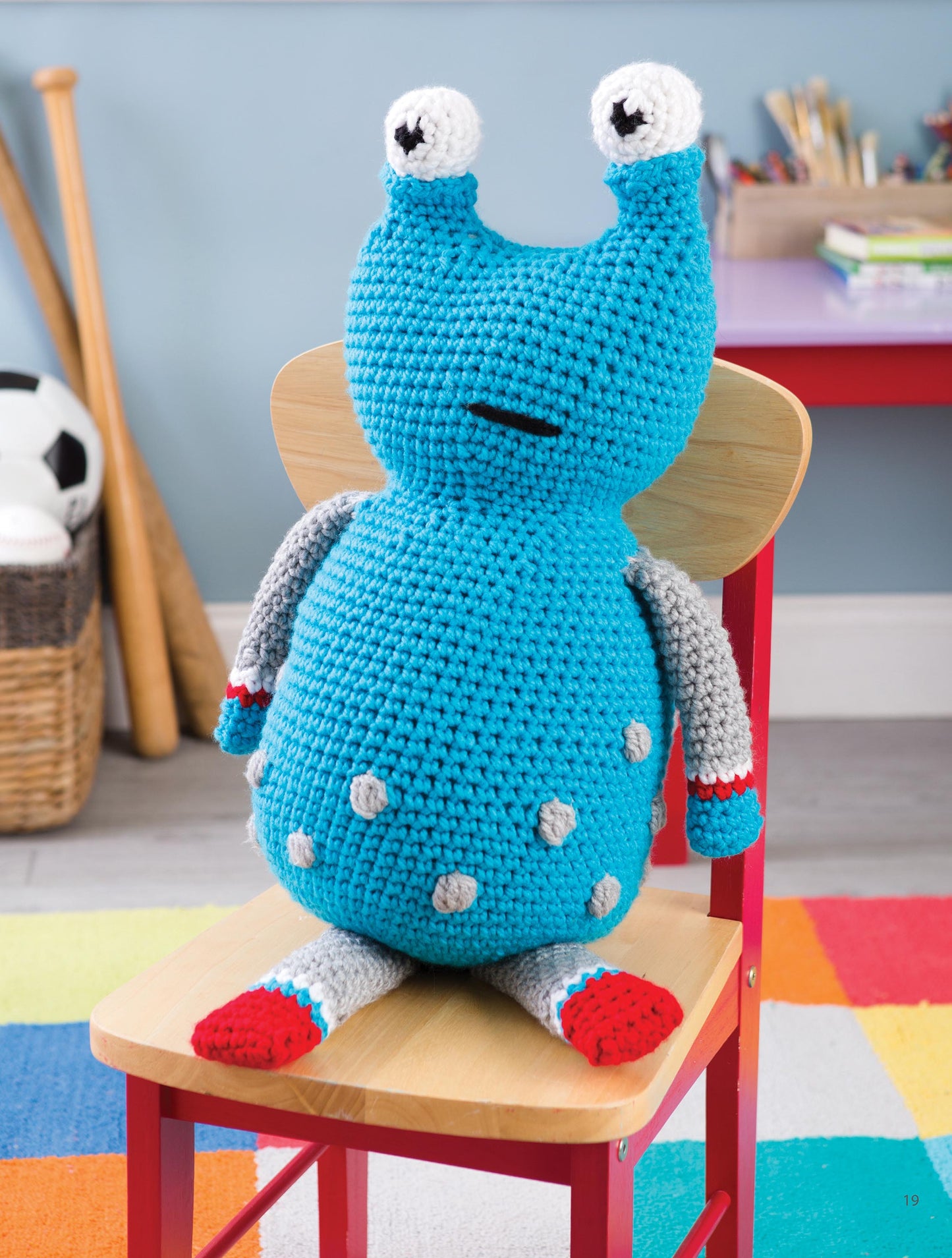 The blue Huggable Monsters toy by Leisure Arts features two eye stalks, gray arms, and red feet. Made from beginner crochet patterns, it’s perfect for kids who love cuddly monsters and playful rooms full of toys and books.
