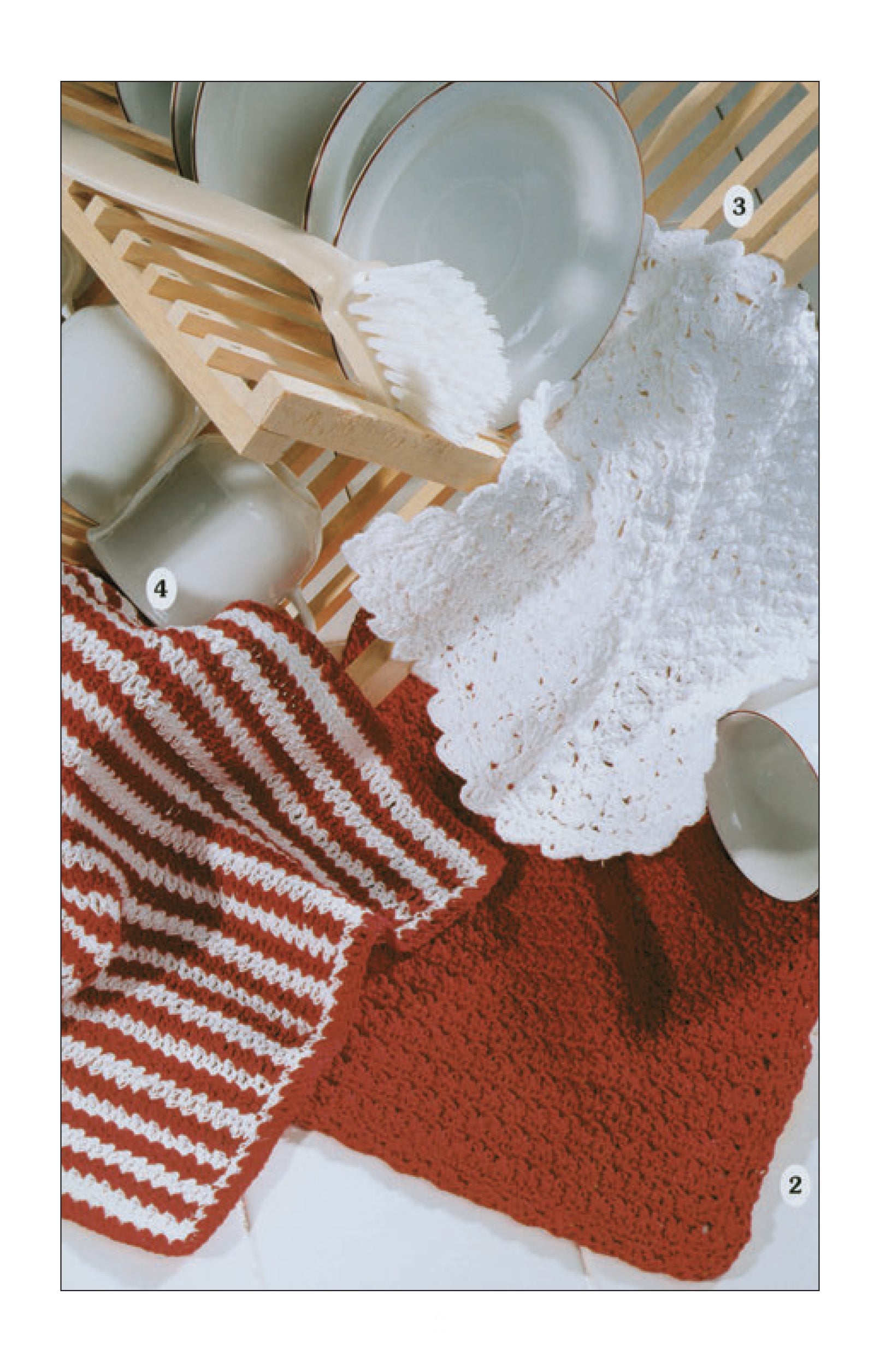 A dish rack holds plates and bowls, with a brush and three Leisure Arts Dishcloths by the Dozen—white, red, and red-and-white striped—nearby, showcasing easy crochet patterns ideal for beginner knitting projects.
