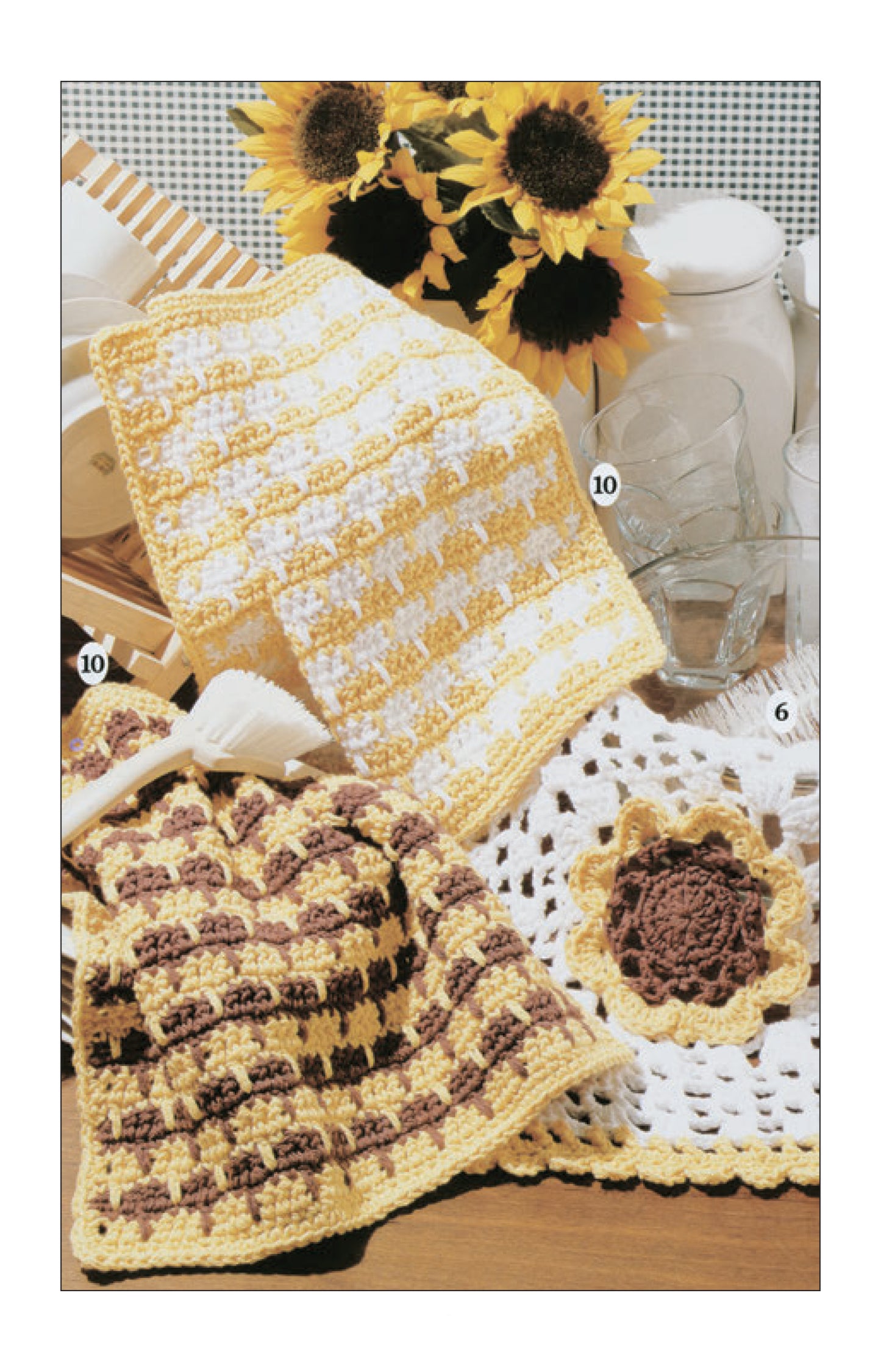 Leisure Arts' Dishcloths by the Dozen, shown in yellow, white, and brown crochet with checkered and floral patterns on wood with sunflowers and glassware, make ideal beginner projects.