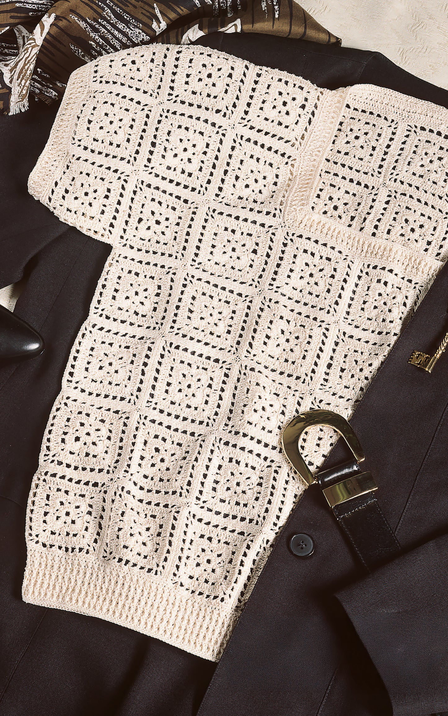 The Thread Crochet—A Beginner's Guide to 9 Projects Digital Download by Leisure Arts inspires this beige, square-patterned crocheted top, styled over a black blazer with gold details; a brown and white scarf adds contrast in the background.