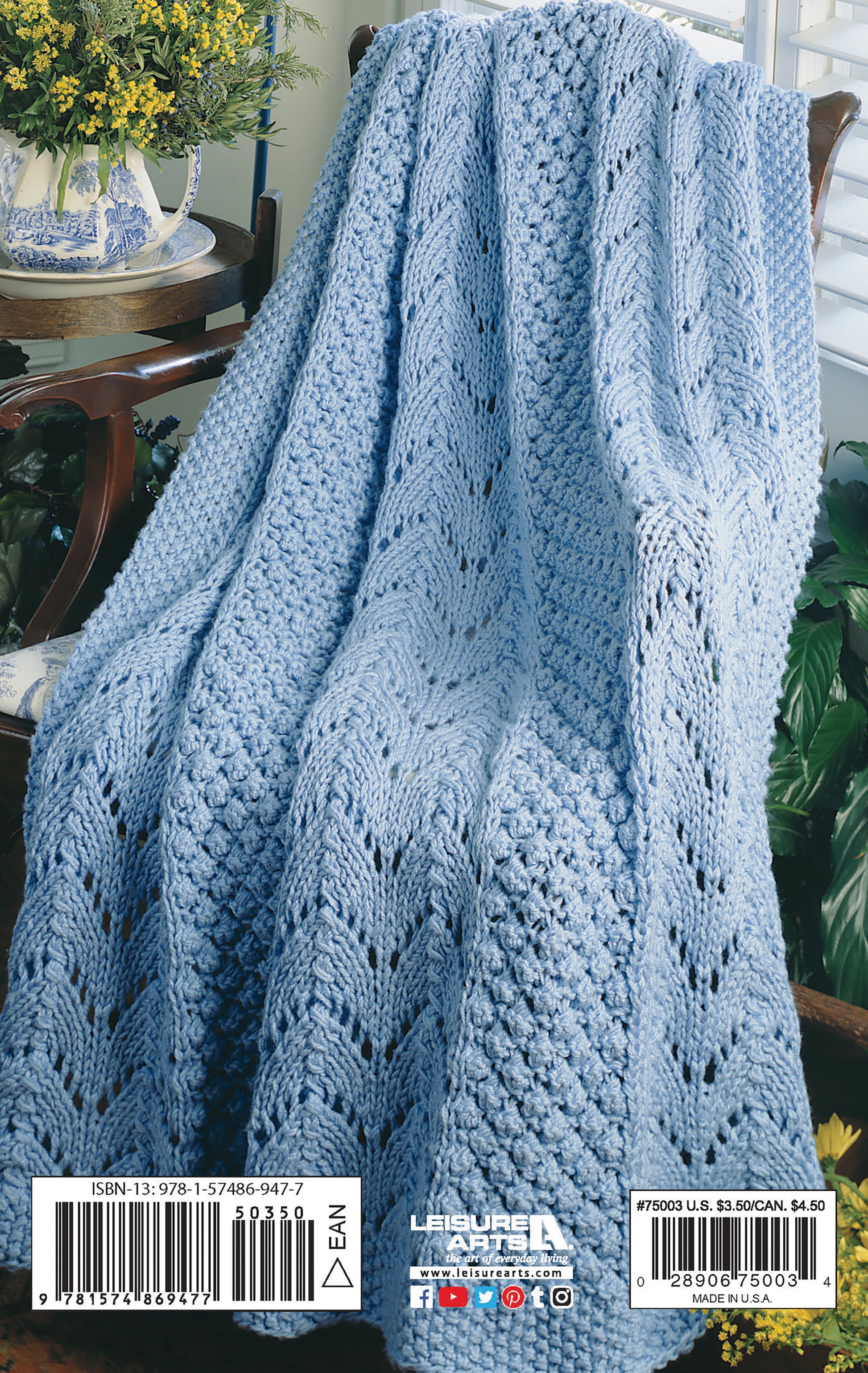 A light blue hand-knitted afghan, made with patterns from Leisure Arts' "Beginner's Guide Knit Stitches & Easy Projects," is draped over a wooden chair beside a plant and a blue and white teapot on a small table.