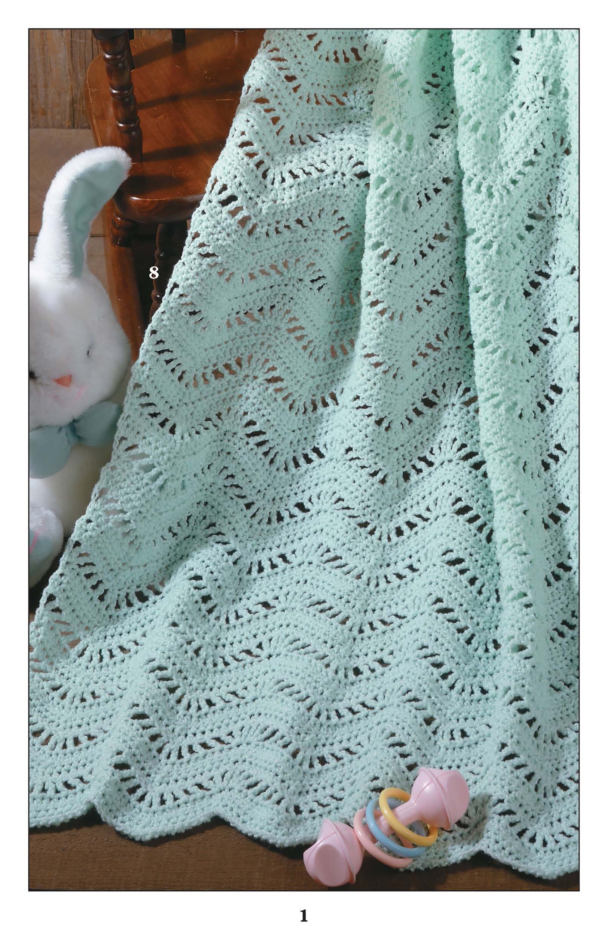 A light blue, lacy knit blanket made from Leisure Arts' "Ripples for Baby to Crochet" pattern is draped over a wooden chair, with a white plush bunny and pastel baby rattle nearby.