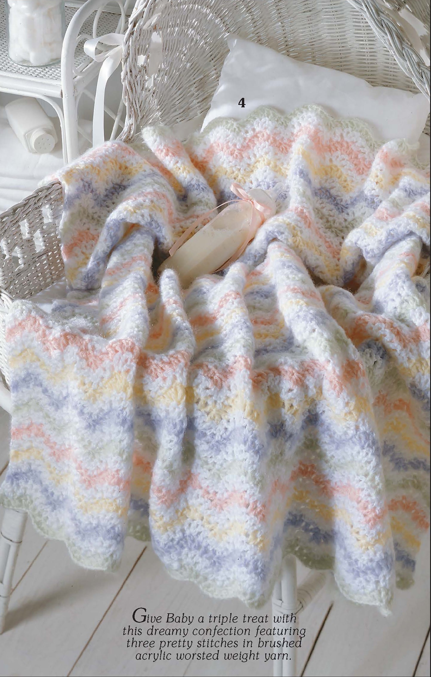 The Ripples for Baby to Crochet by Leisure Arts—a pastel chevron baby blanket in brushed acrylic yarn—drapes over a wicker chair topped with ballet slippers, creating a cozy nursery scene inspired by crochet patterns.