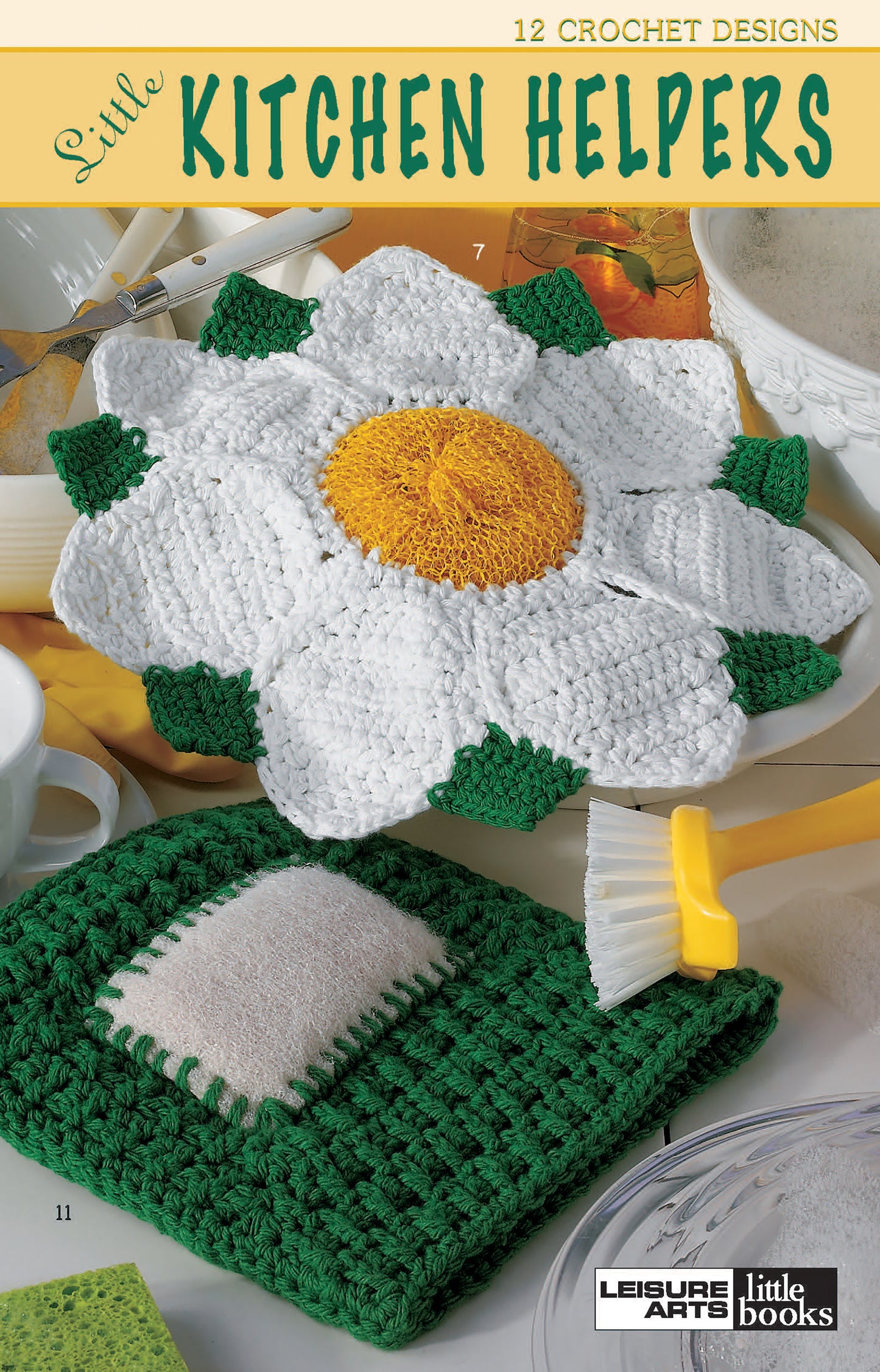 A white and yellow daisy dish scrubber and a green and white dishcloth sit on a kitchen counter. Text: Little Kitchen Helpers by Leisure Arts—12 crochet designs for perfect gifts or kitchen projects.